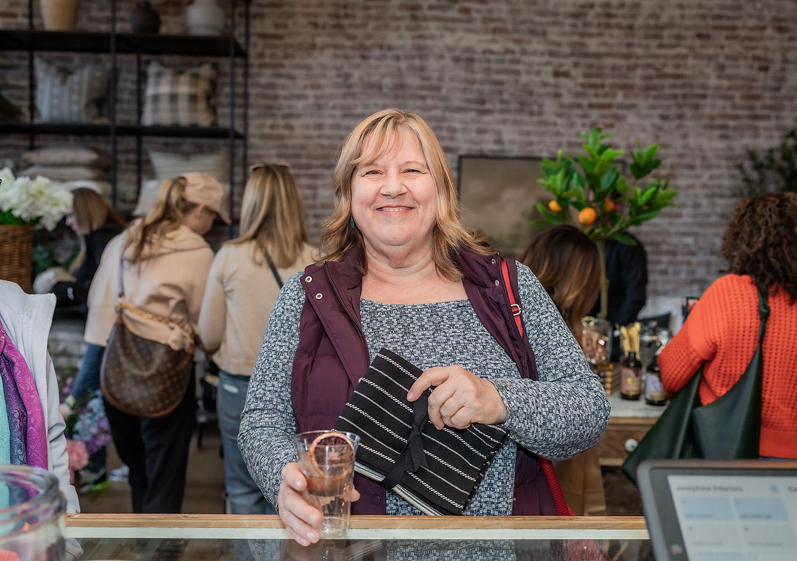 A woman is standing behind a counter in a store holding a glass of wine.