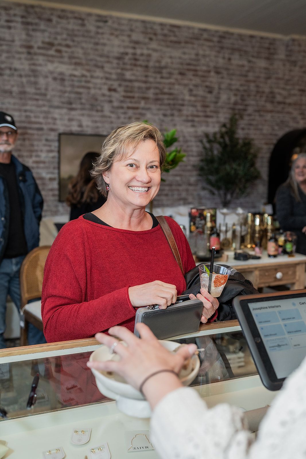 A woman in a red sweater is smiling while standing at a counter in a restaurant.