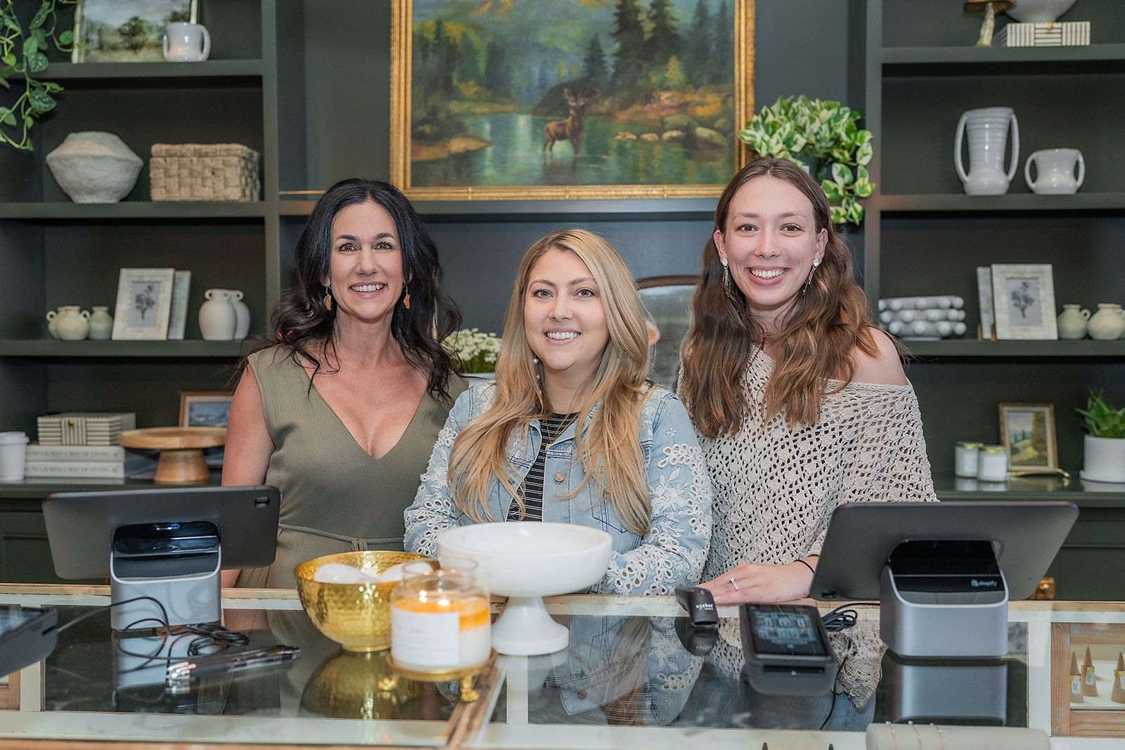 Three women are posing for a picture in front of a counter in a store.
