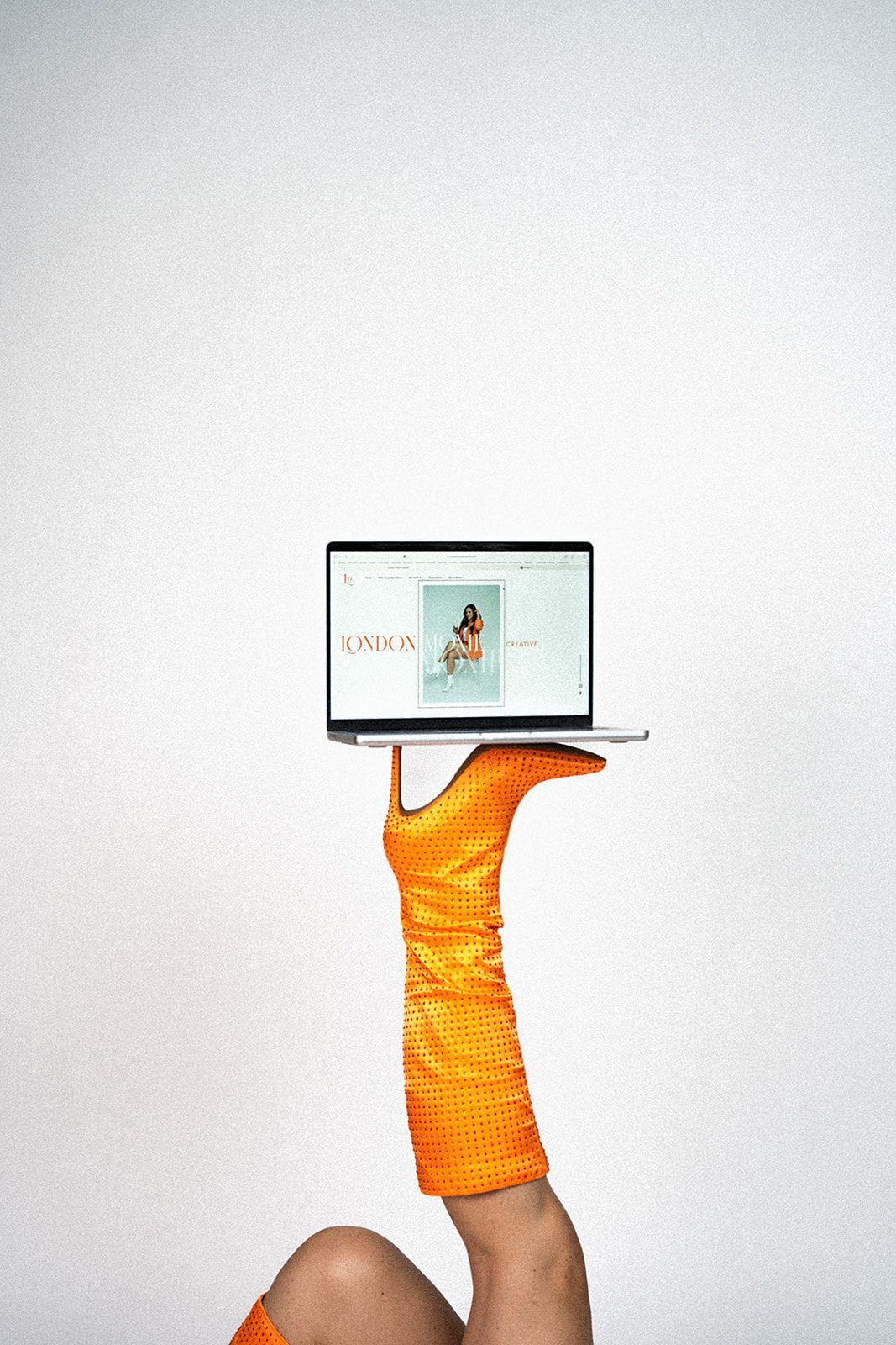A woman in orange boots is holding a laptop in her hand.