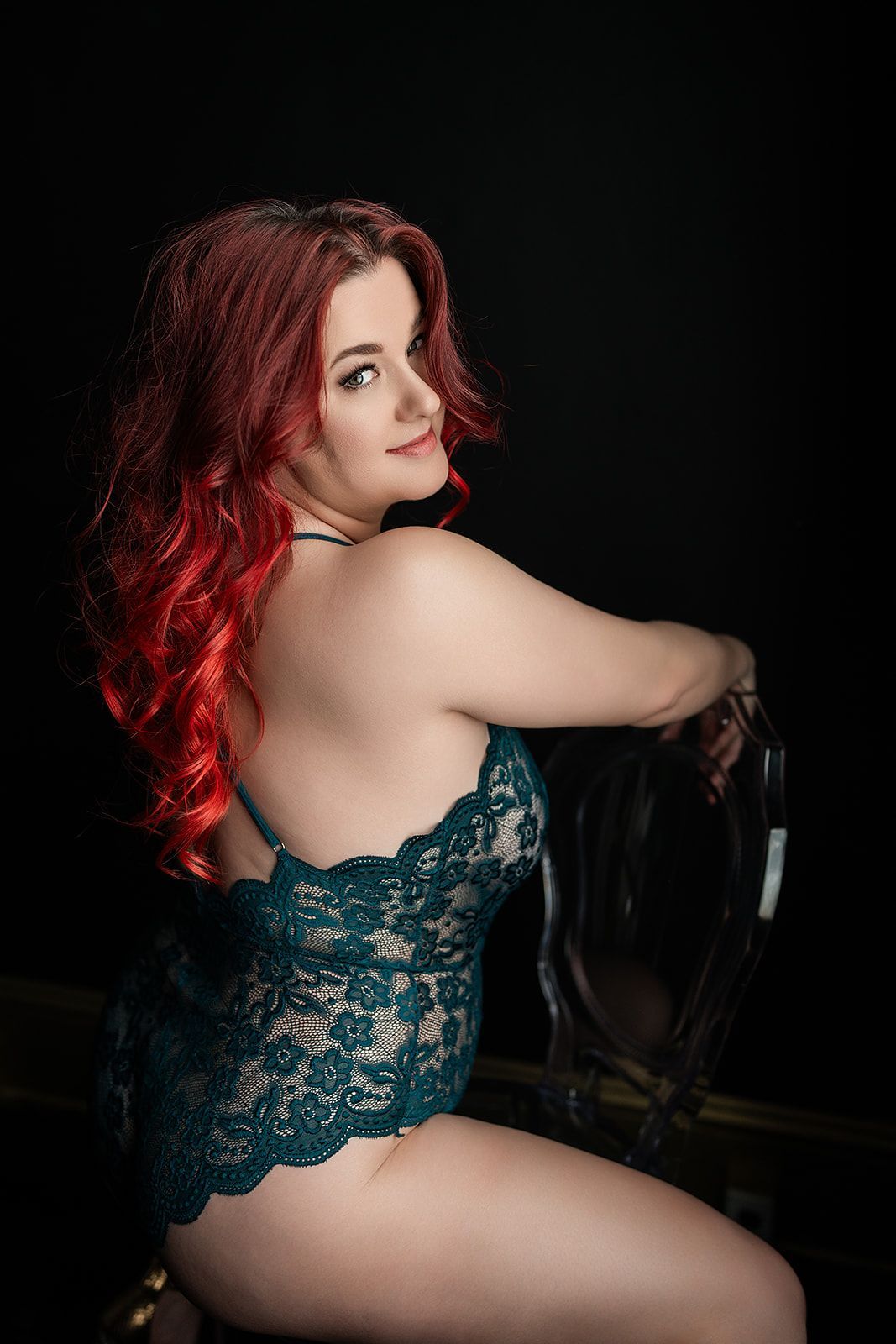 A woman with red hair is sitting on a chair in lingerie.