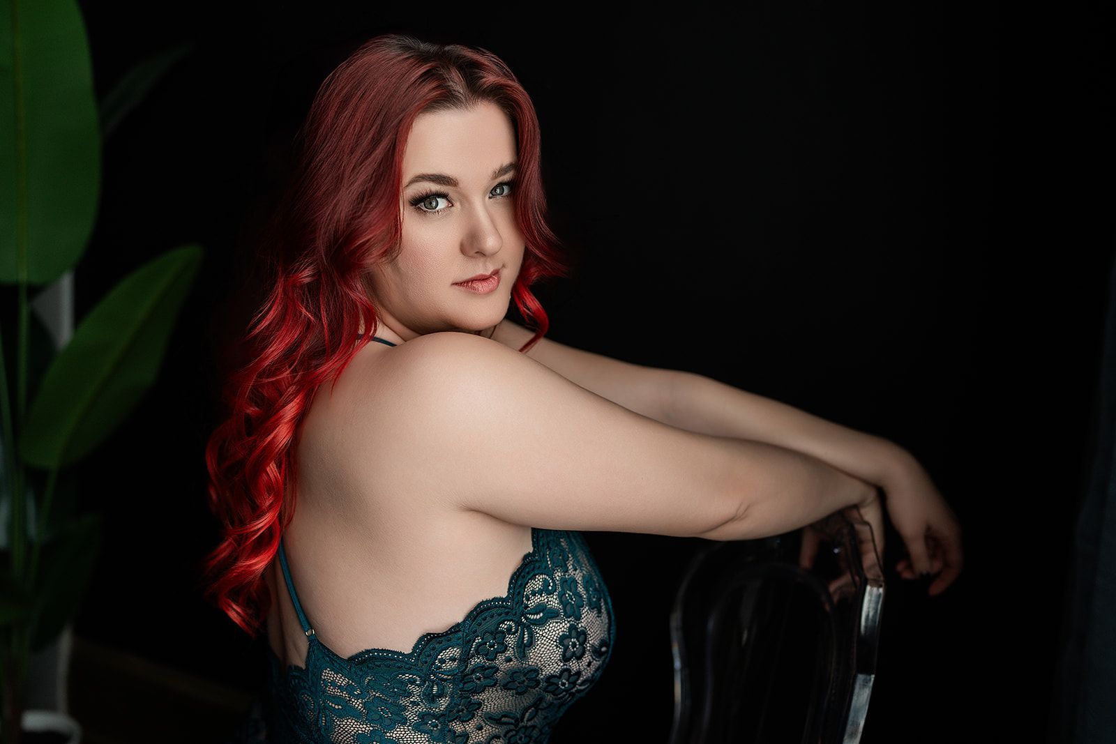 A woman with red hair is sitting on a chair in lingerie.