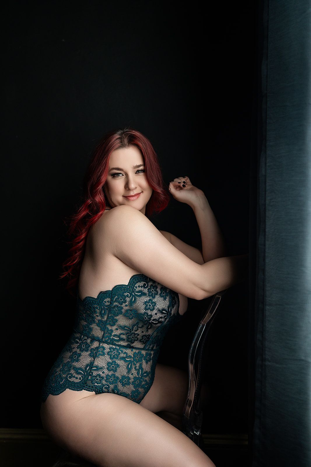 A woman in lingerie is sitting on a chair in front of a window.