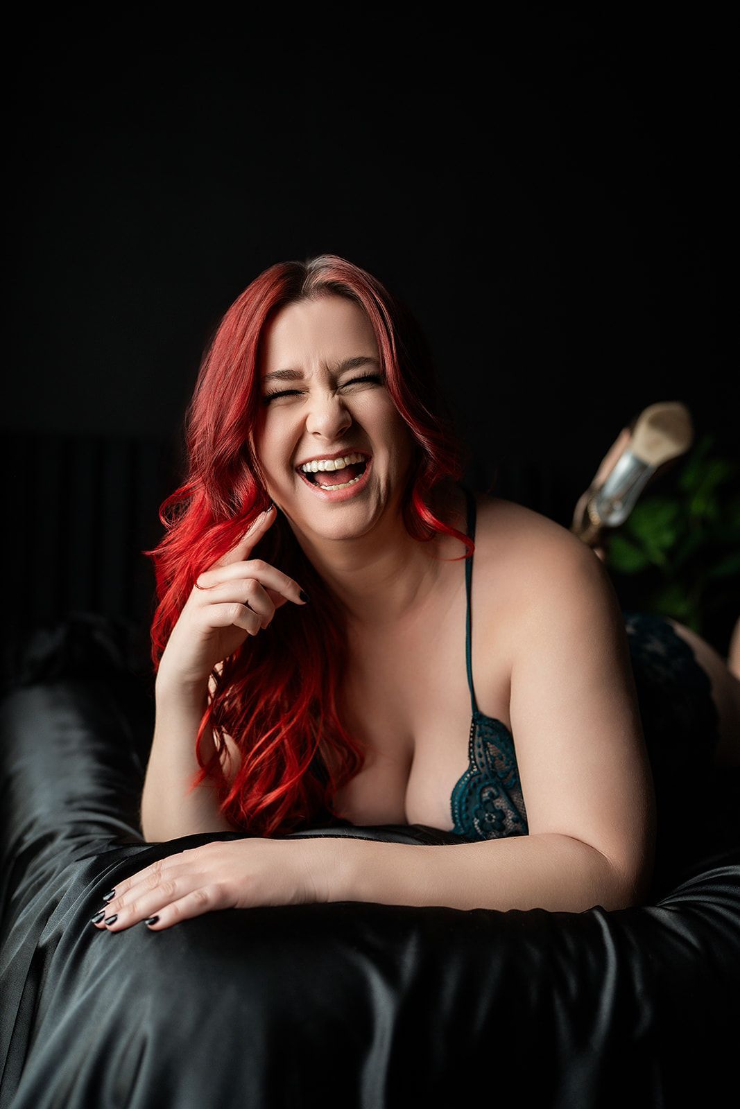 A woman with red hair is laying on a bed and laughing for a boudoir photo shoot in Medford, Oregon