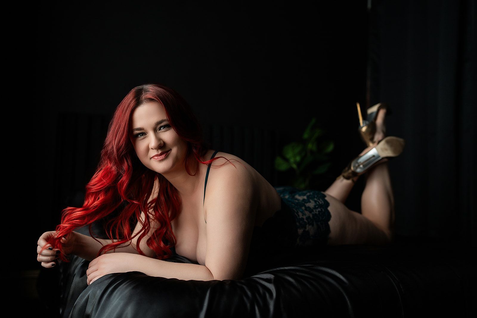 A woman with red hair is laying on her stomach on a bed  for a boudoir photo shoot in Medford, Oregon.
