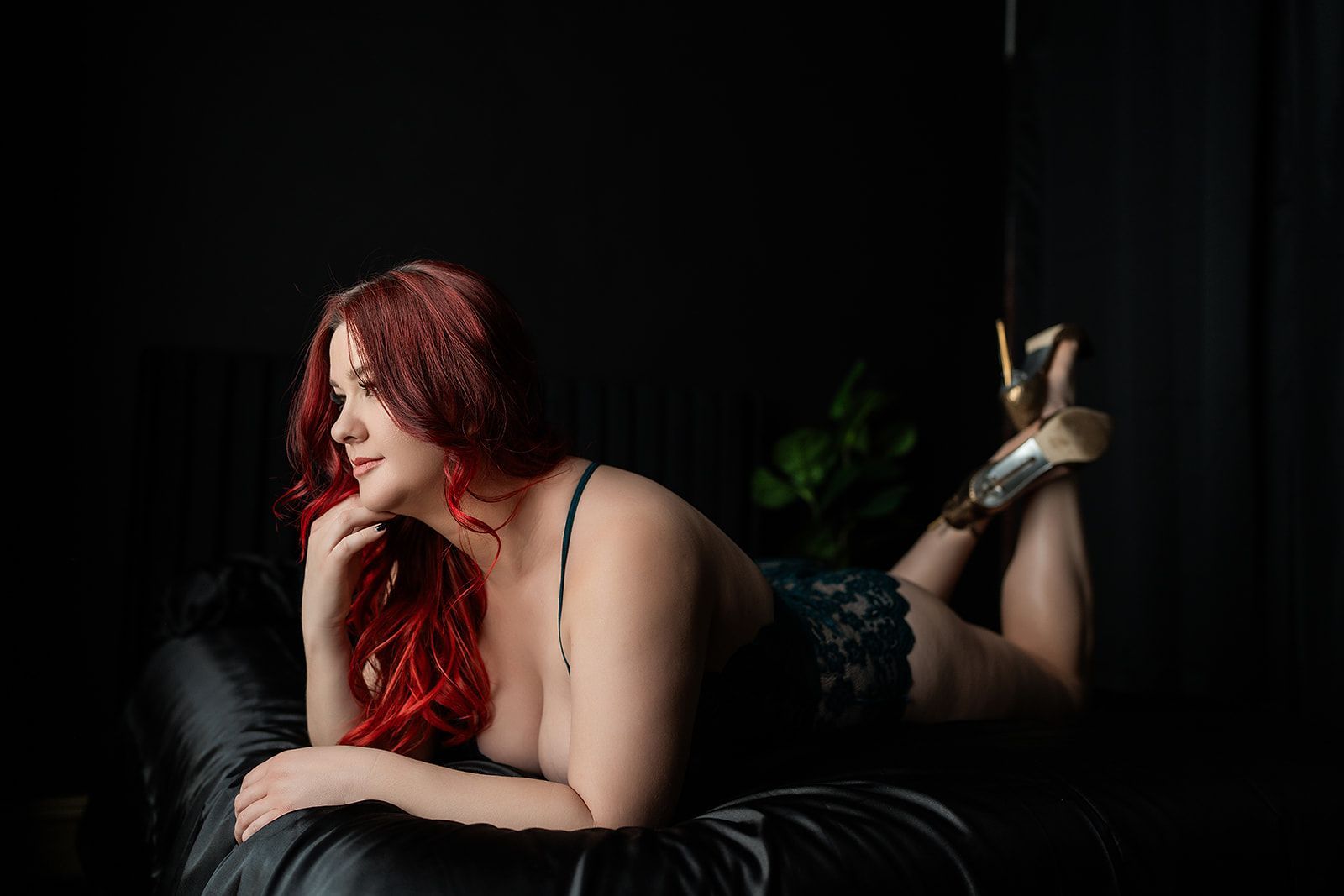 A woman with red hair is laying on a bed in lingerie for a boudoir photo shoot in Medford, Oregon