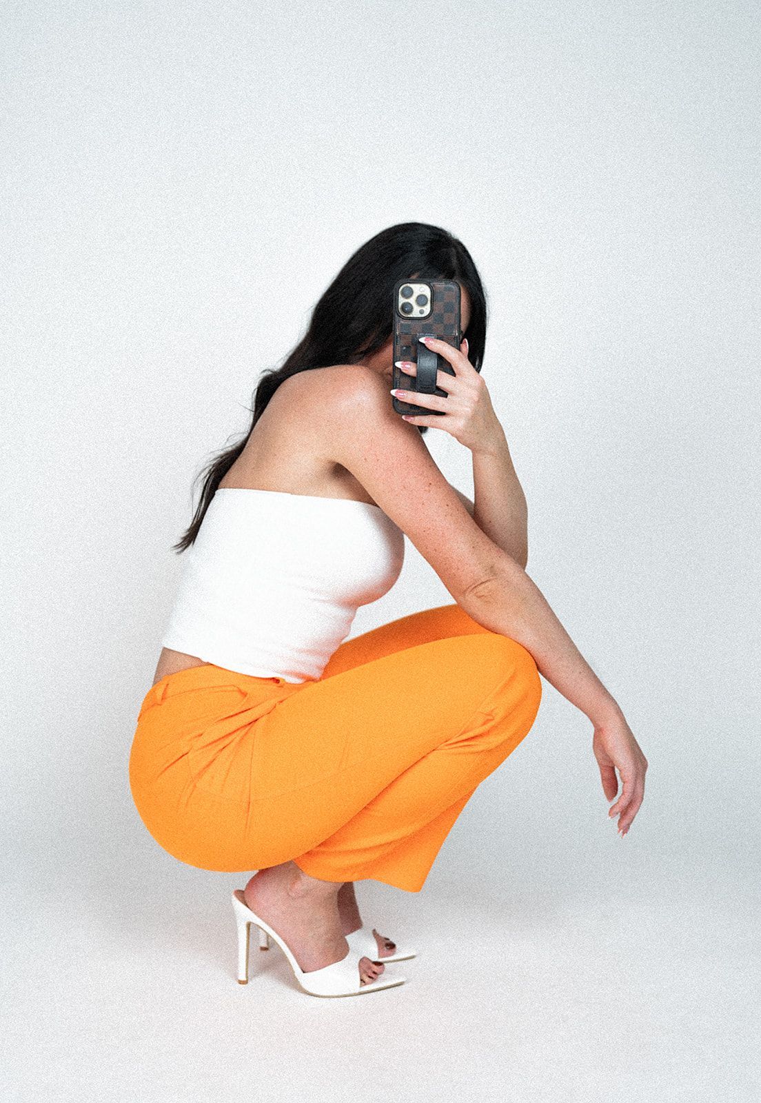 A woman is squatting down taking a selfie with her phone.