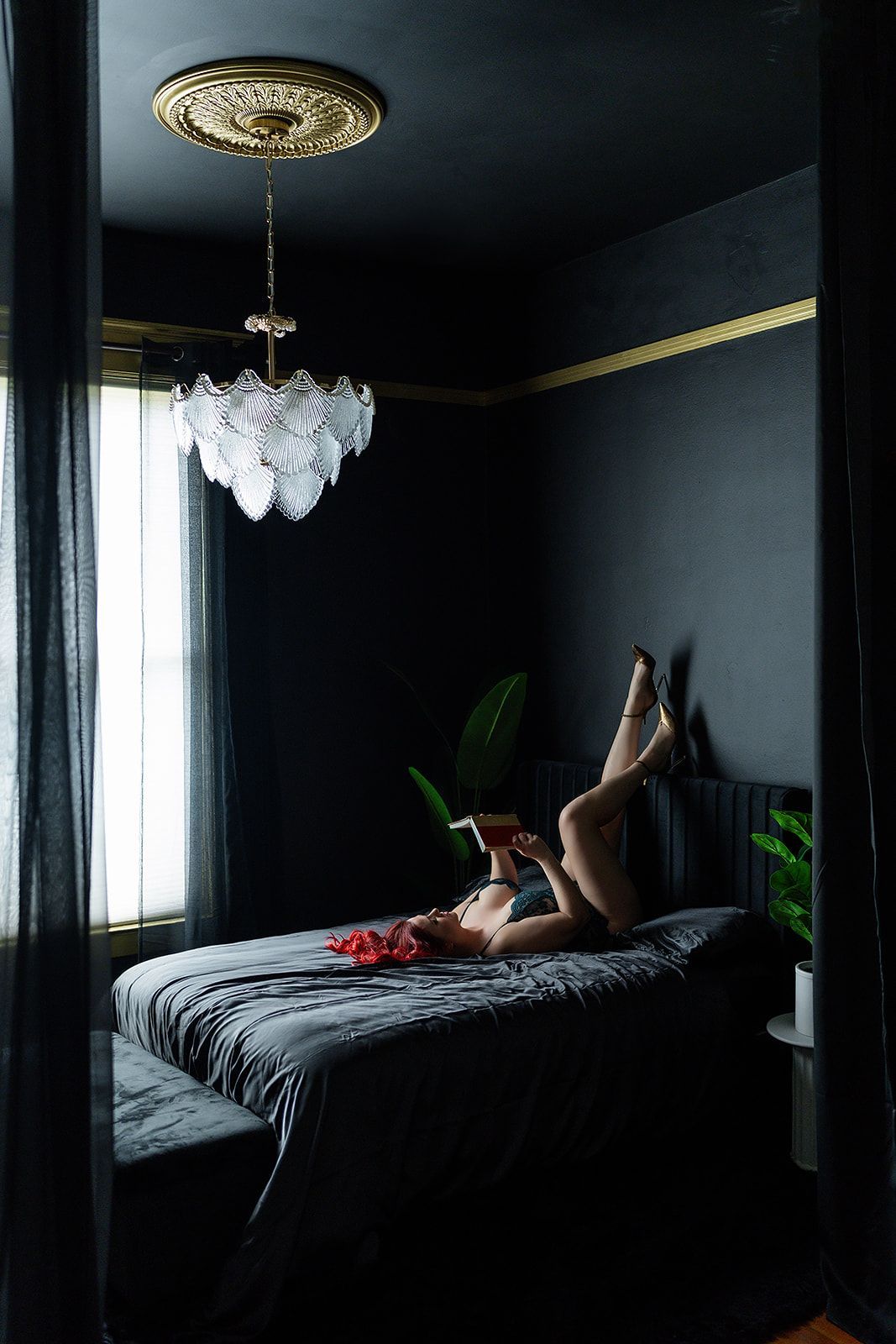 A woman is laying on her stomach on a bed in a dark room for a boudoir photo shoot in Medford, Oregon