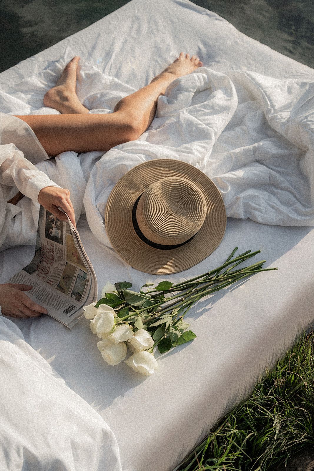 A woman is laying on a bed reading a newspaper.