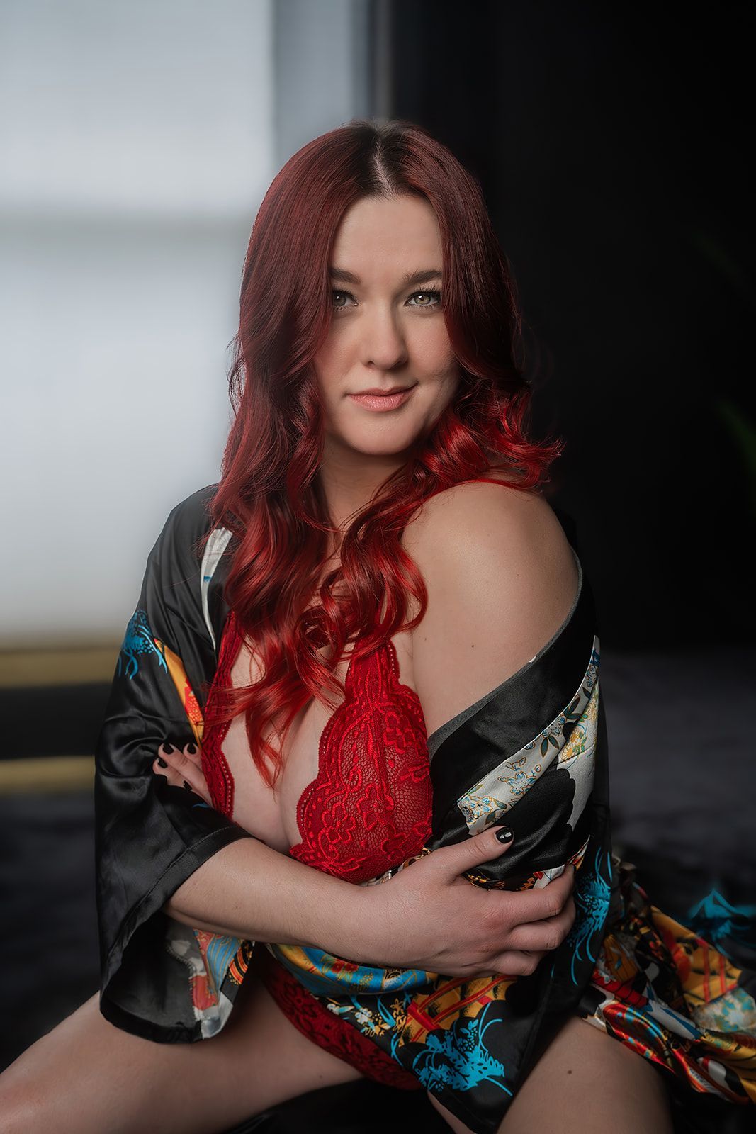 A woman with red hair is wearing a kimono and a red bra for a boudoir photo shoot in Medford, Oregon