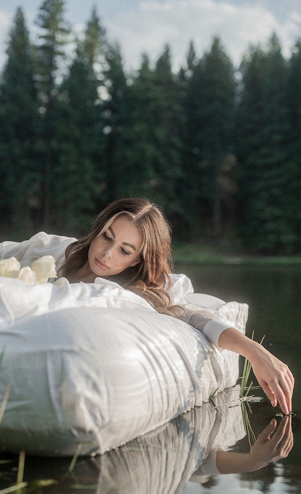 A woman is laying on a white pillow in the water.