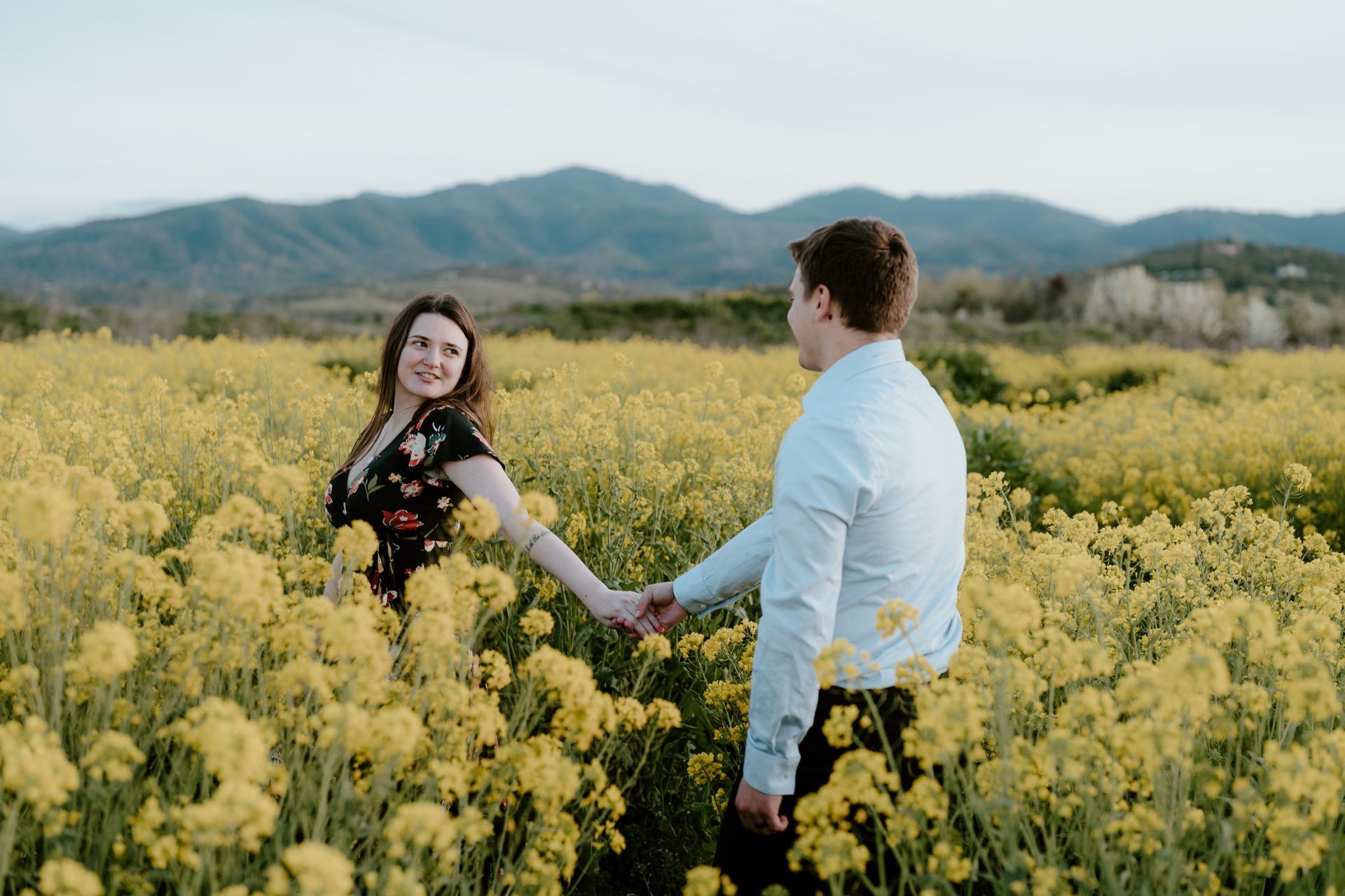 A man and a woman are holding hands in a field of yellow flowers.