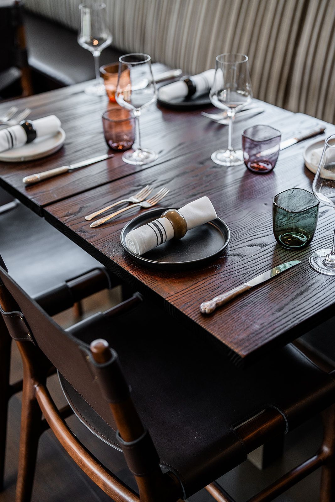 A wooden table with plates , glasses , silverware and napkins on it.