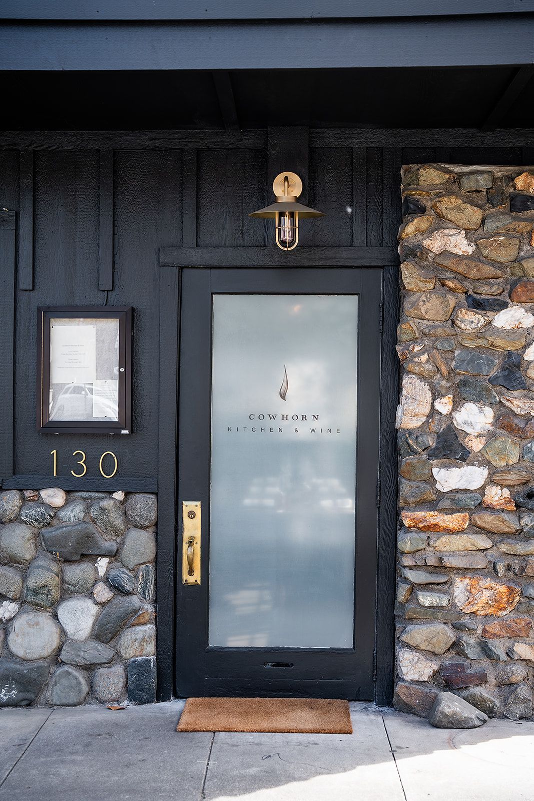 A black door with a glass door is surrounded by a stone wall.
