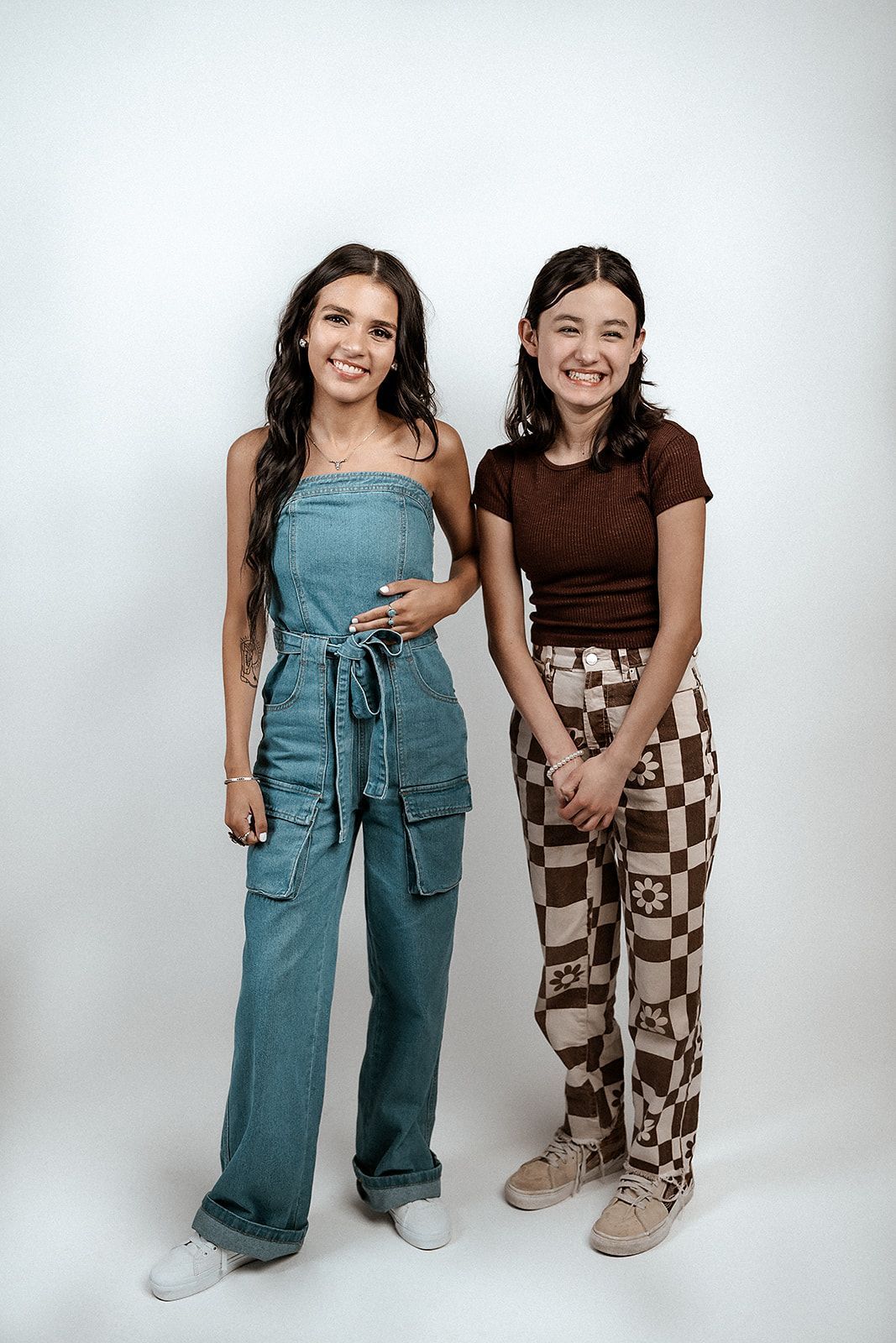 Two young women are standing next to each other on a white background.