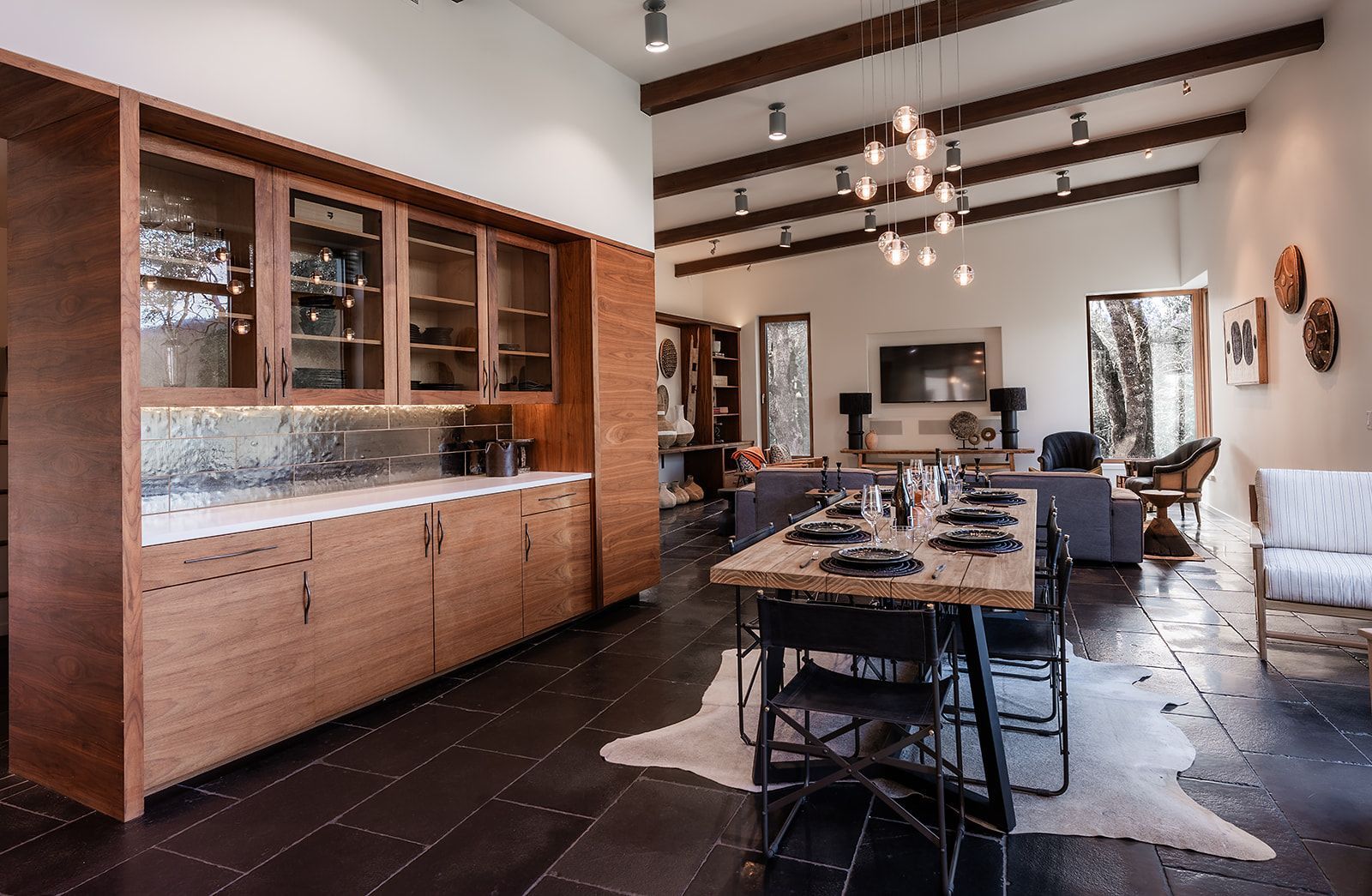 Modern open-plan living space with kitchen cabinetry, a dining table, and a living area with a fireplace and a rug.