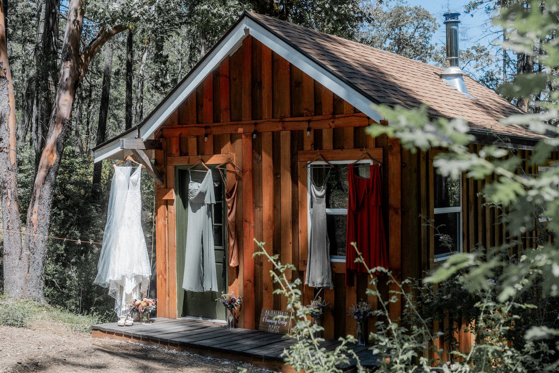 A small wooden cabin in the woods with dresses hanging on the door.