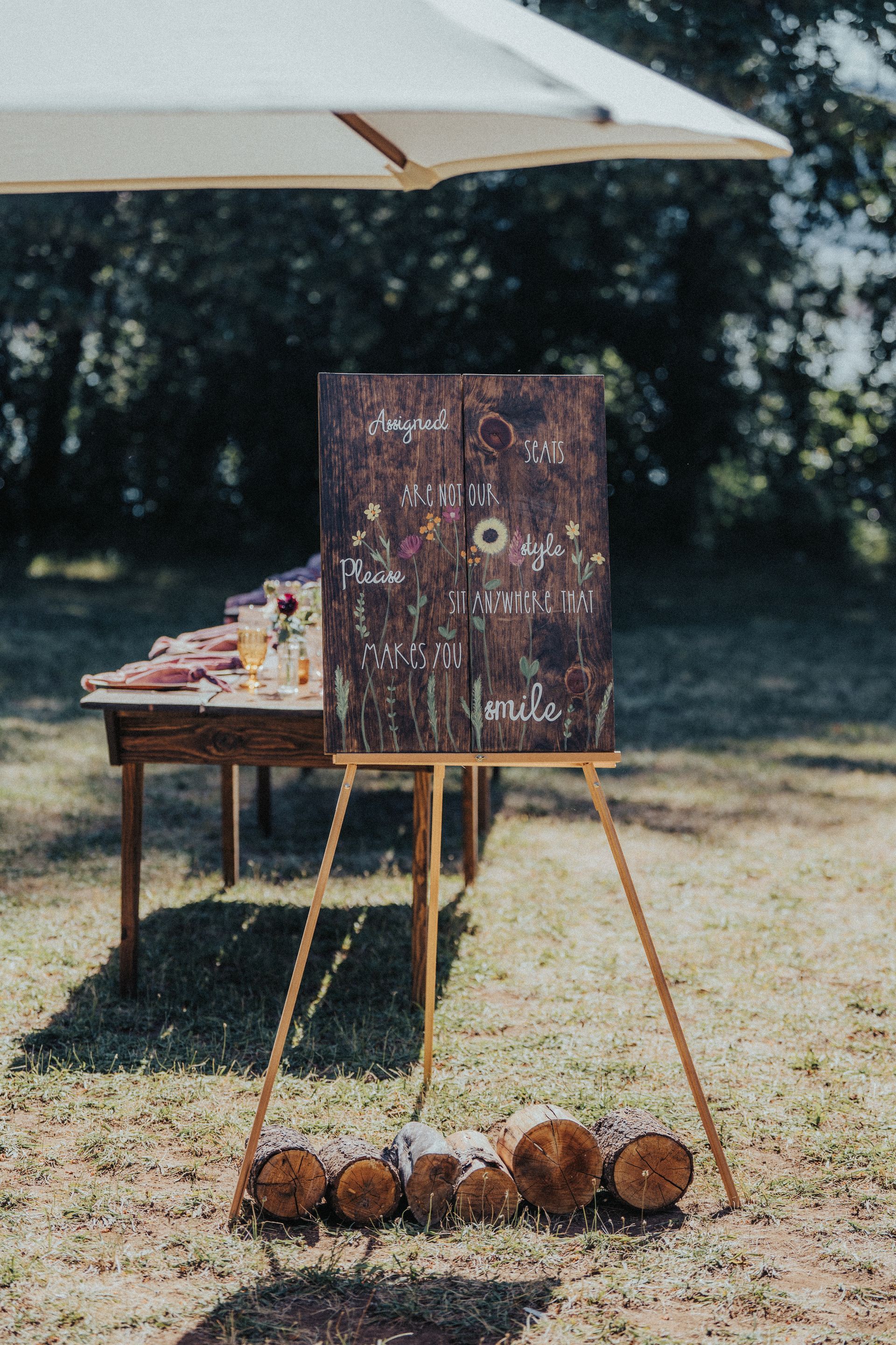 A wooden easel with a sign on it is sitting in the grass under an umbrella.