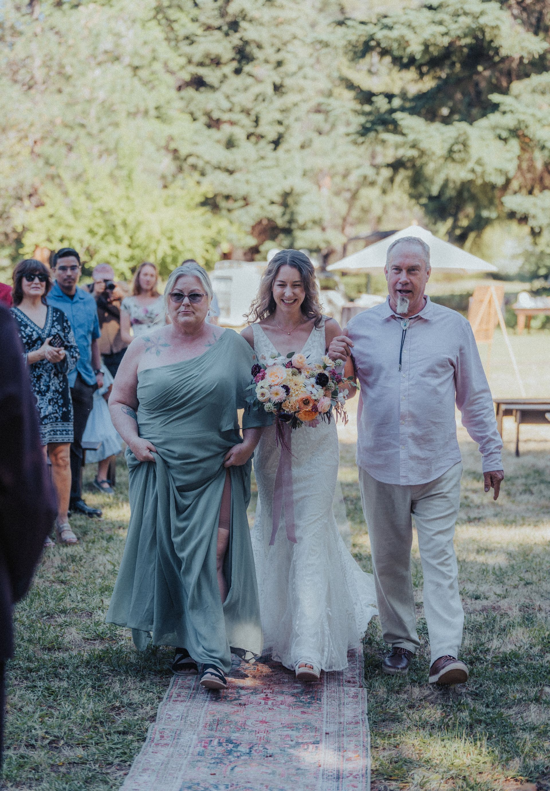 A bride is walking down the aisle with her parents at her wedding.