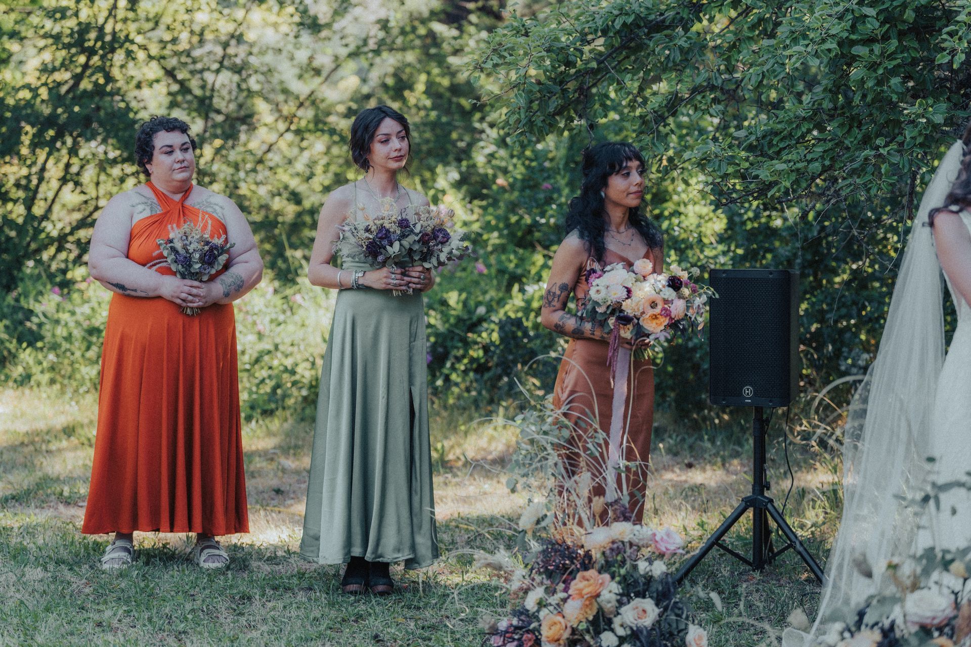 A bride and her bridesmaids are standing in a field holding bouquets of flowers.