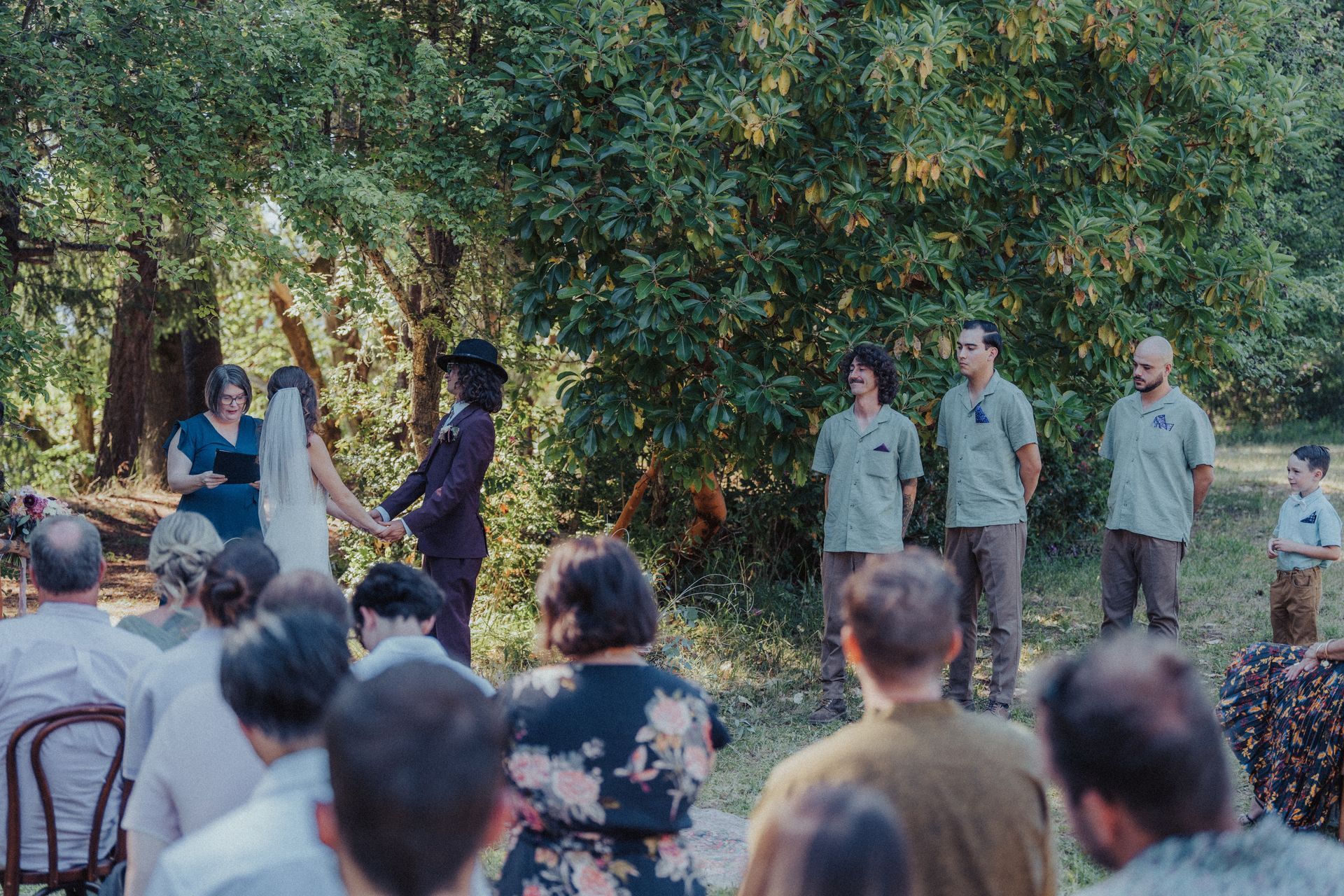 A bride and groom are holding hands during their wedding ceremony in front of a crowd of people.