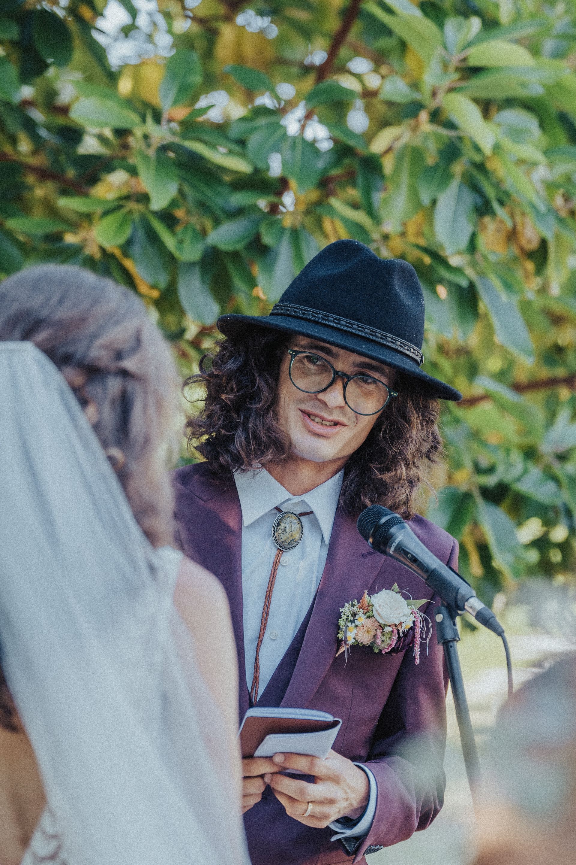 A man in a suit and hat is giving a speech to a bride.