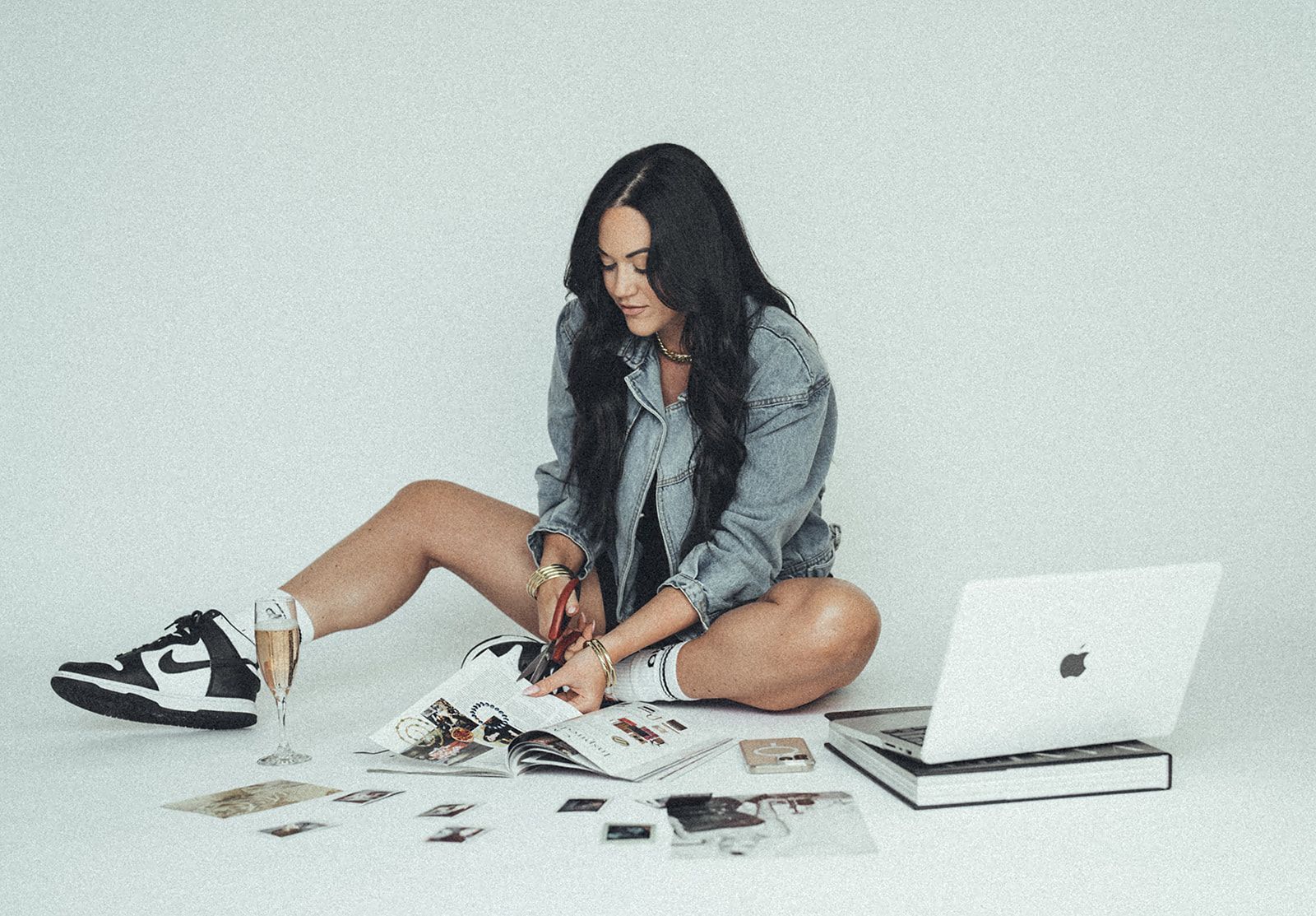 A woman is sitting on the floor reading a magazine next to a laptop.