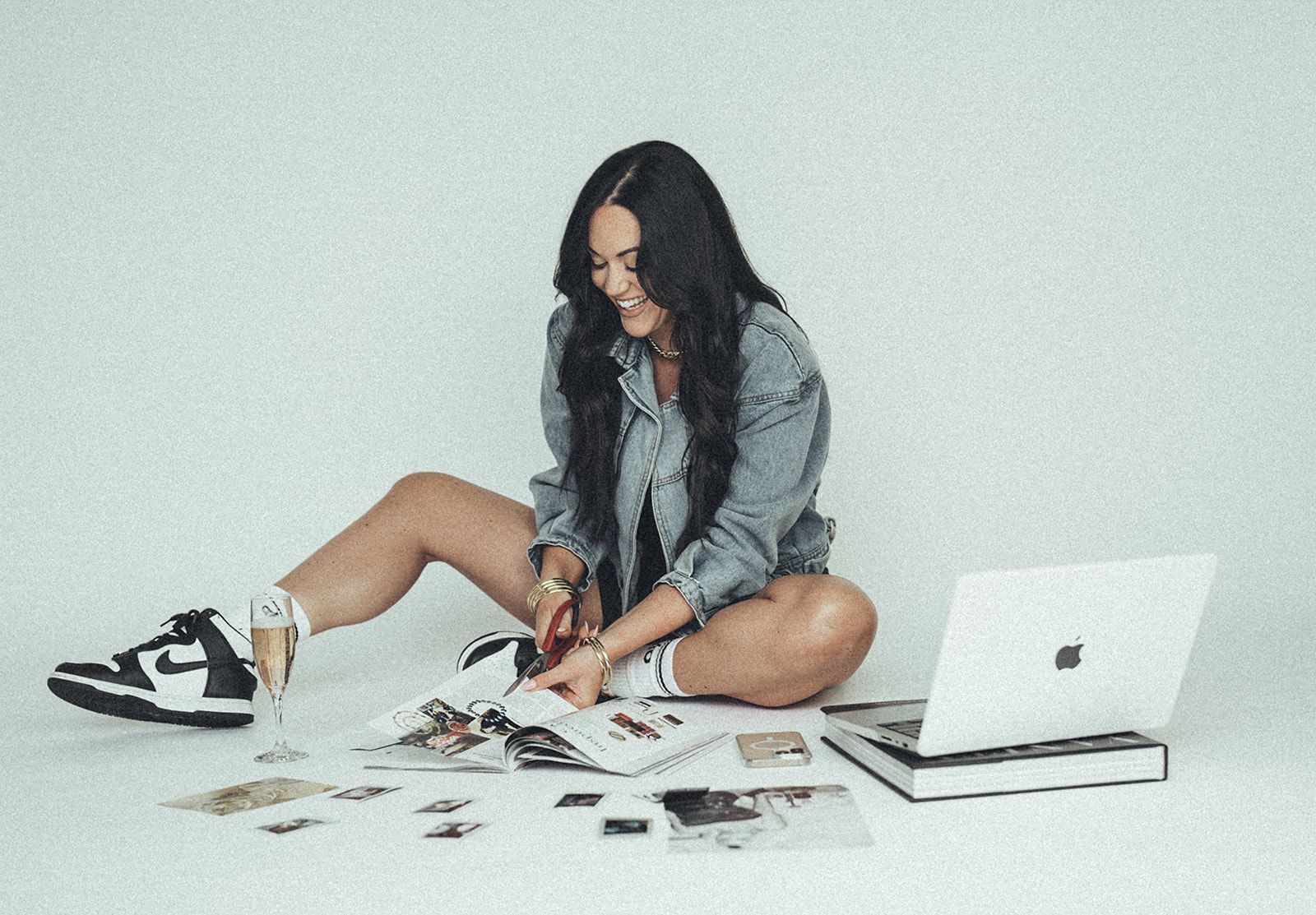 A woman is sitting on the floor with a laptop and a magazine.