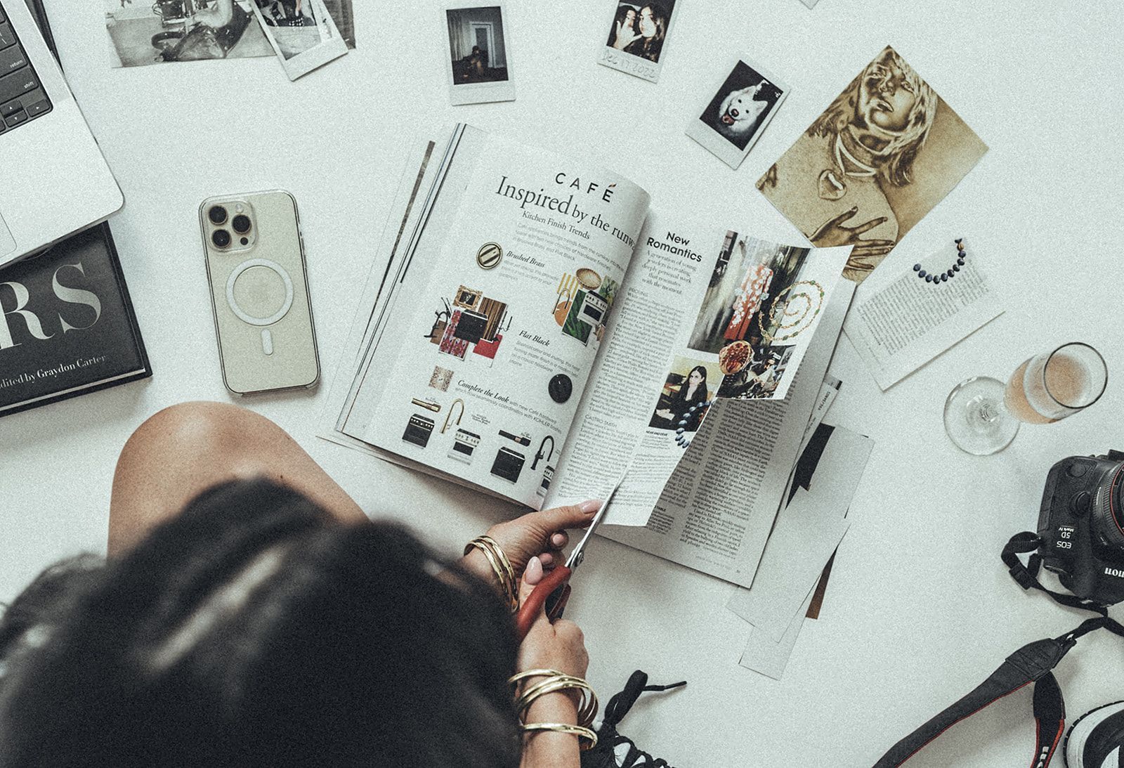 A woman is sitting at a table cutting a magazine with scissors.