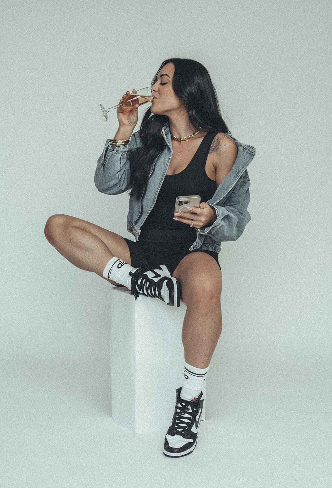 A woman is sitting on a cube drinking from a glass.