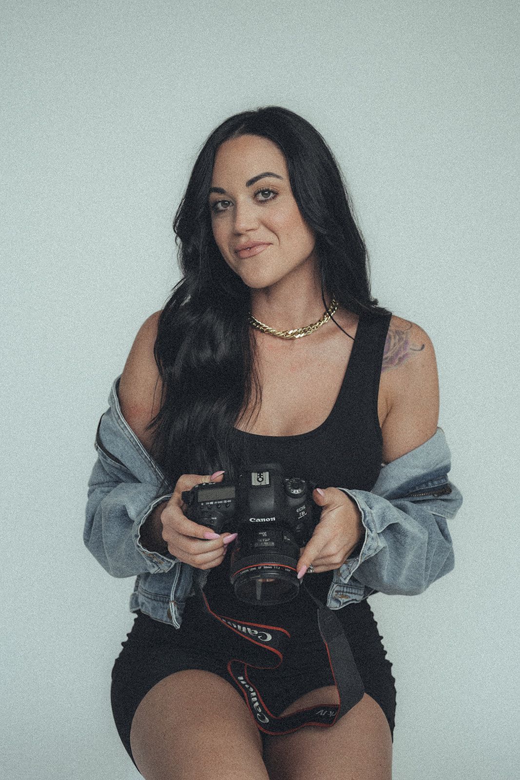 A woman in a black dress and denim jacket is holding a camera.