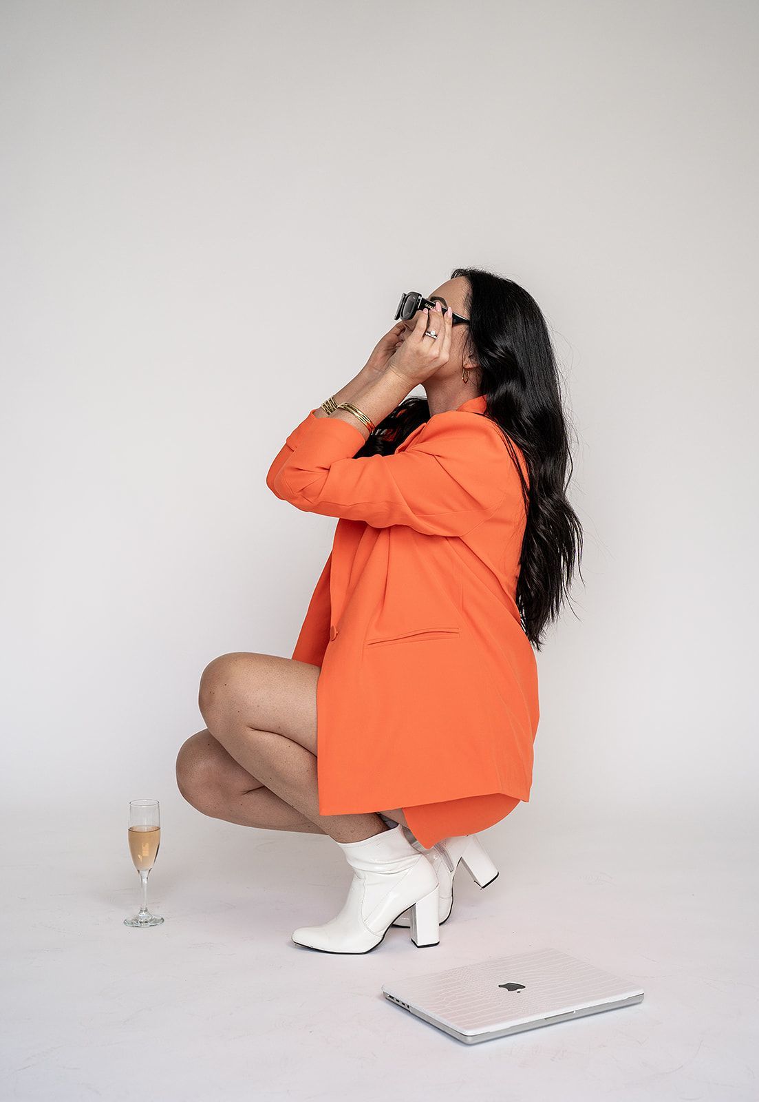 A woman in an orange suit is kneeling down with a glass of champagne.