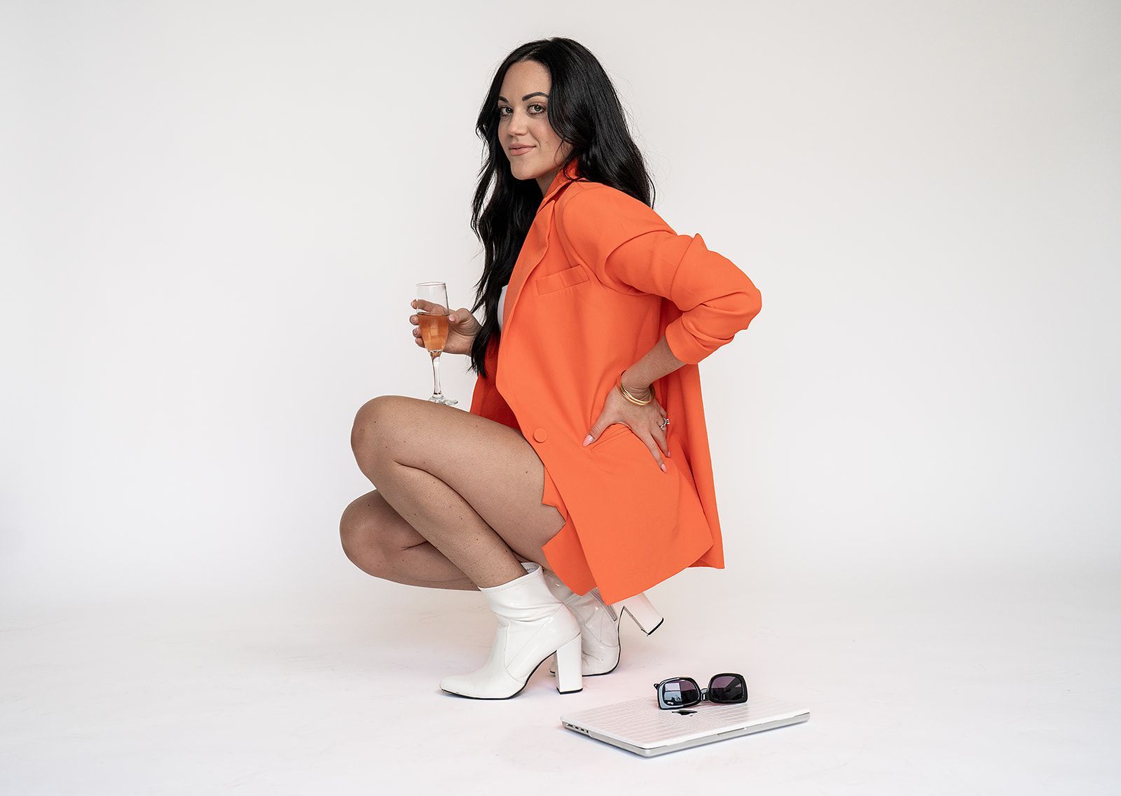 A woman is squatting down while holding a glass of wine.