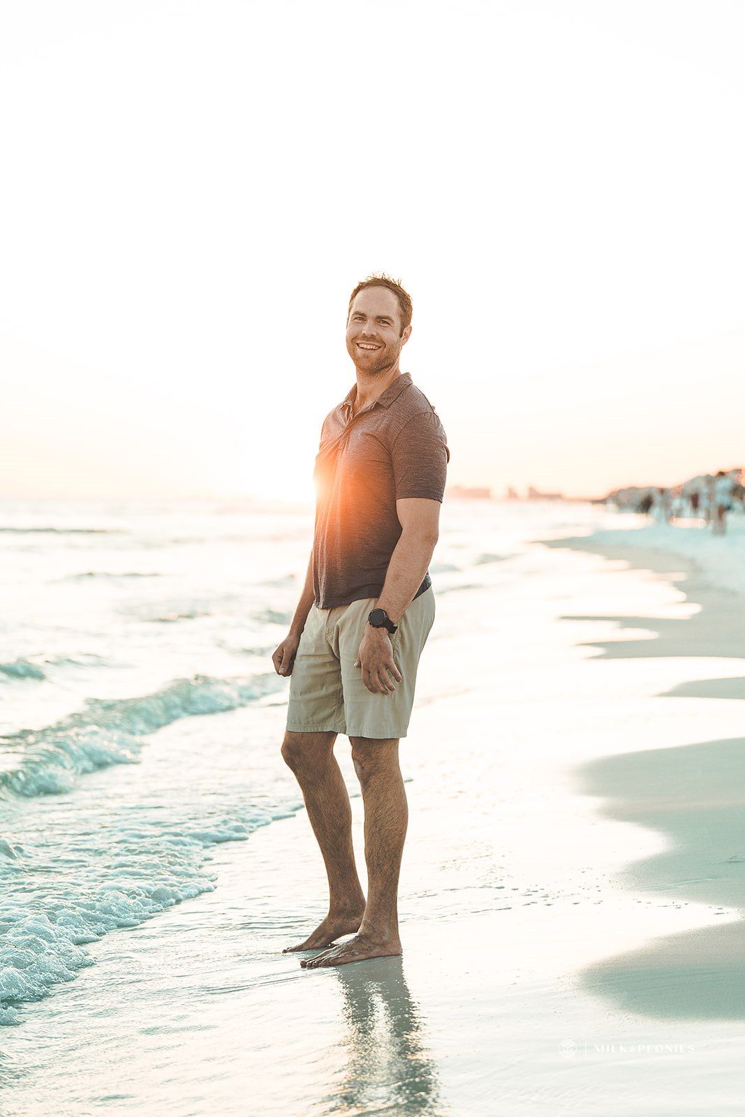 A man is standing on the beach looking at the ocean.