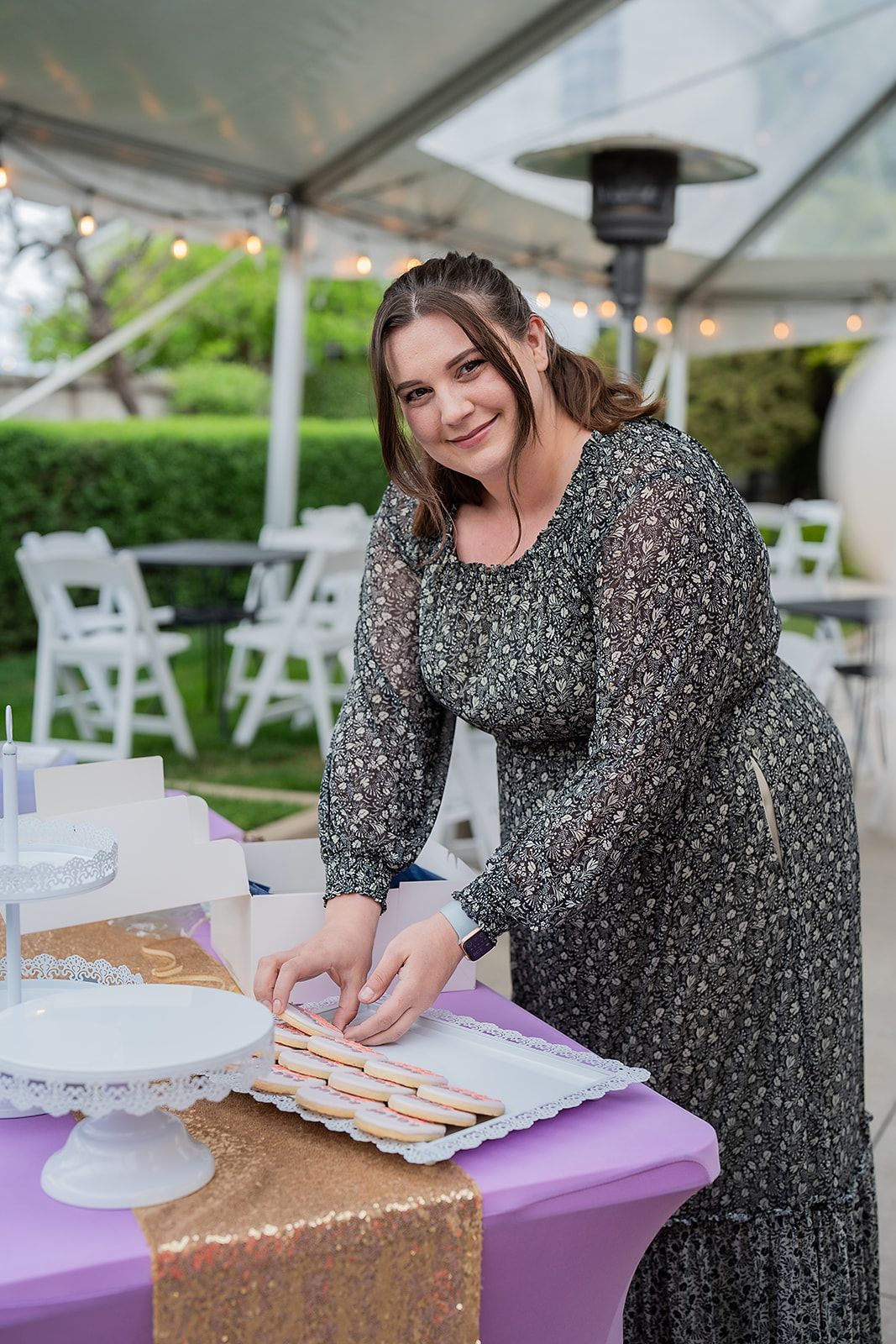 A woman in a dress is standing at a table cutting a cake.