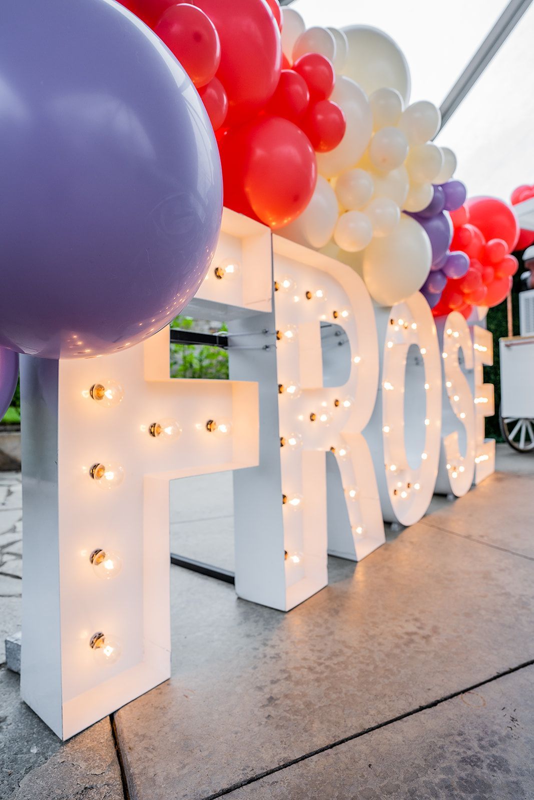 A large white letter f is surrounded by balloons and lights.