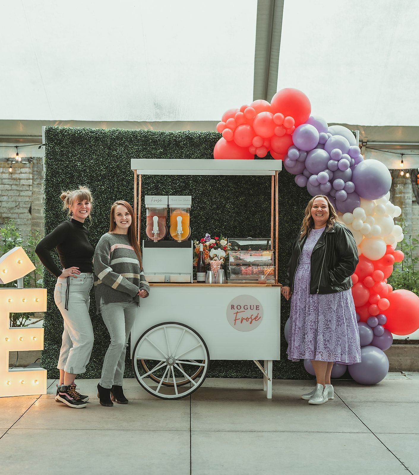 Three women are standing in front of a cart decorated with balloons.