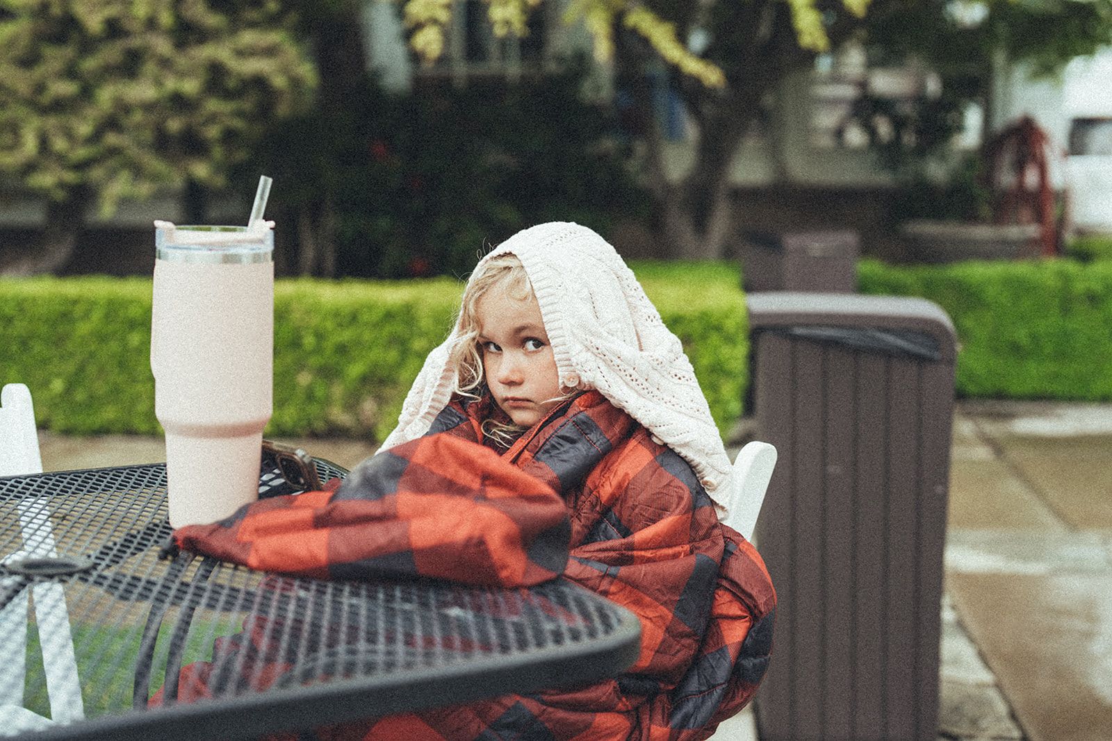 A little girl is sitting at a table wrapped in a blanket.