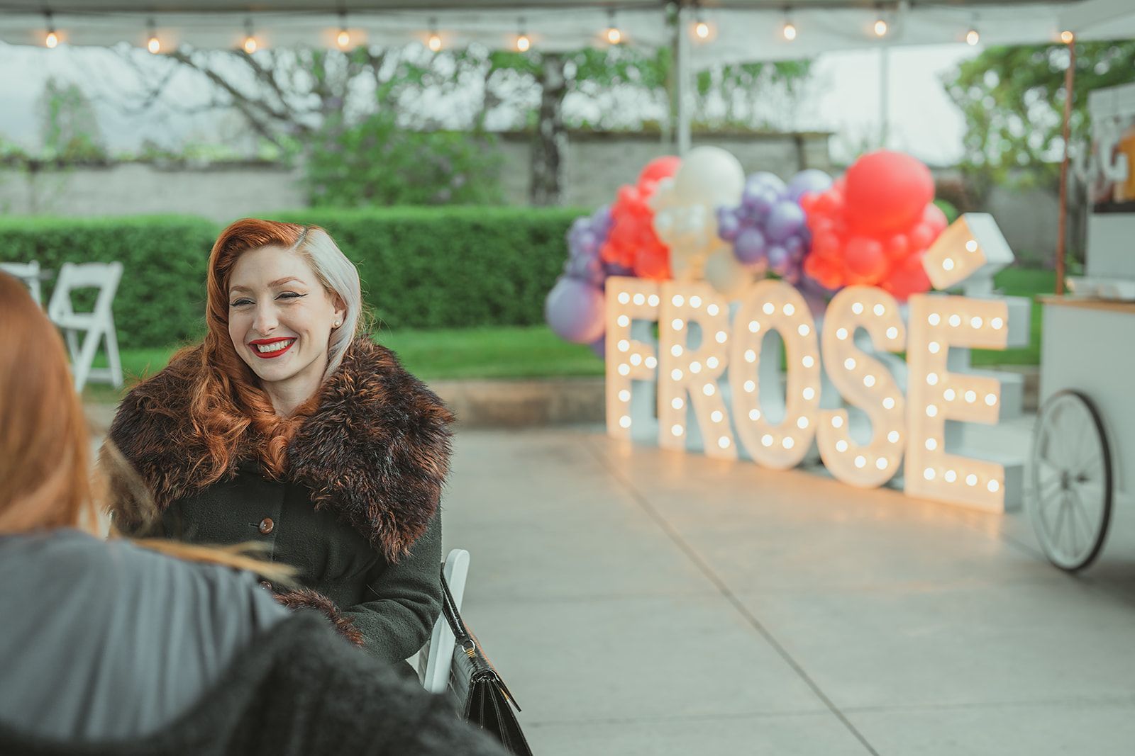 A woman is sitting in front of a sign that says `` rose ''.