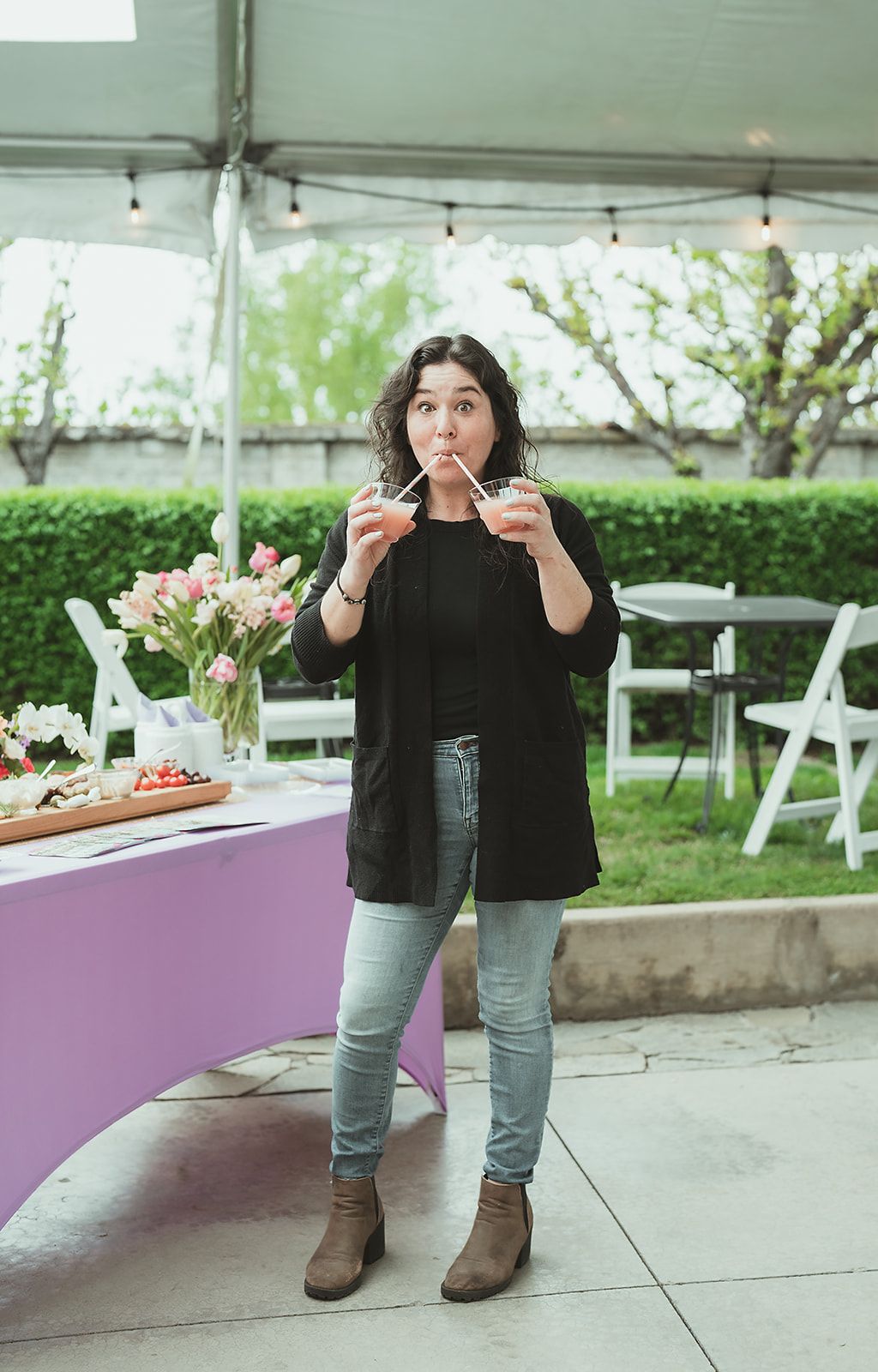 A woman is drinking a drink while standing in front of a table.