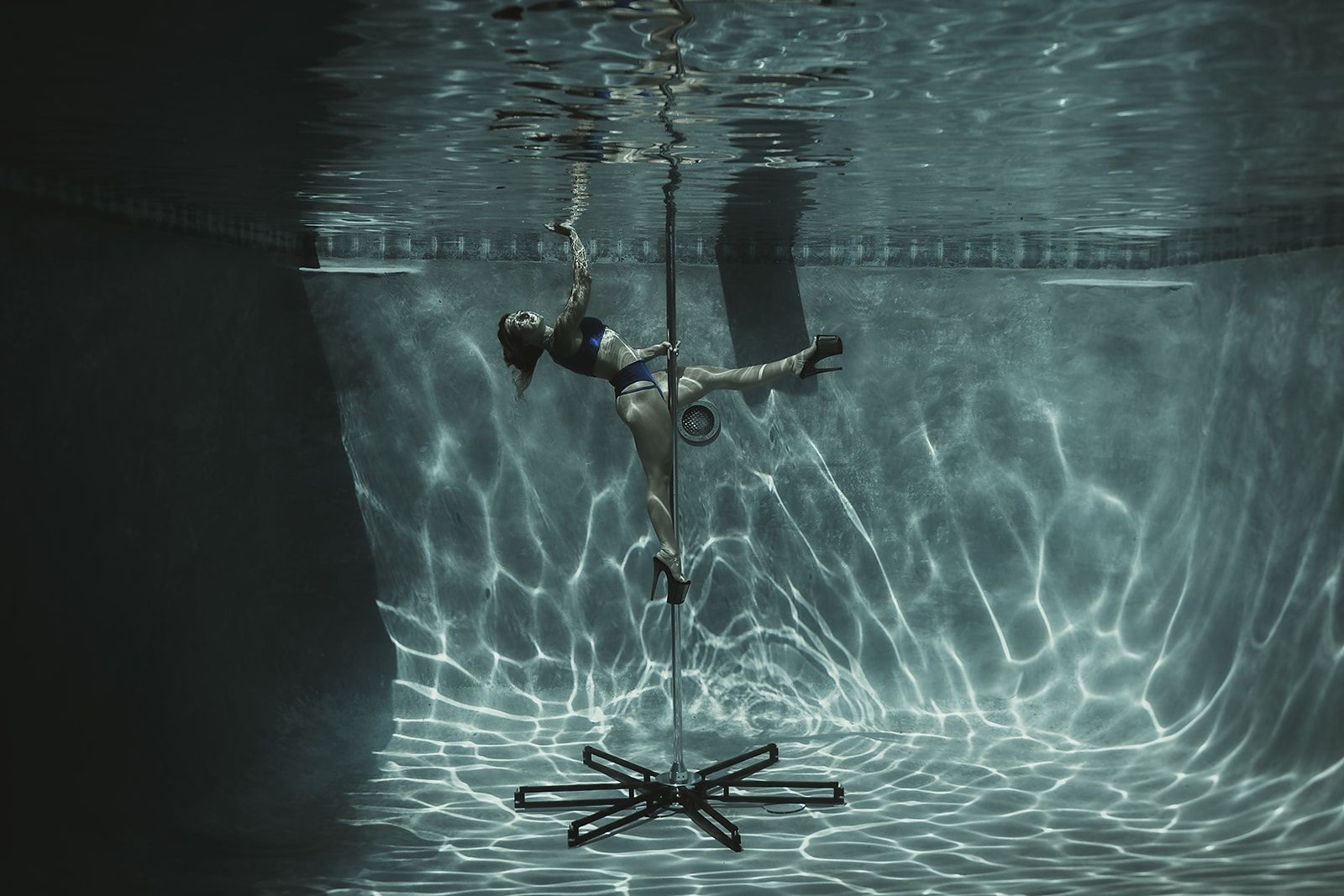 A woman is standing on a pole underwater in a pool.