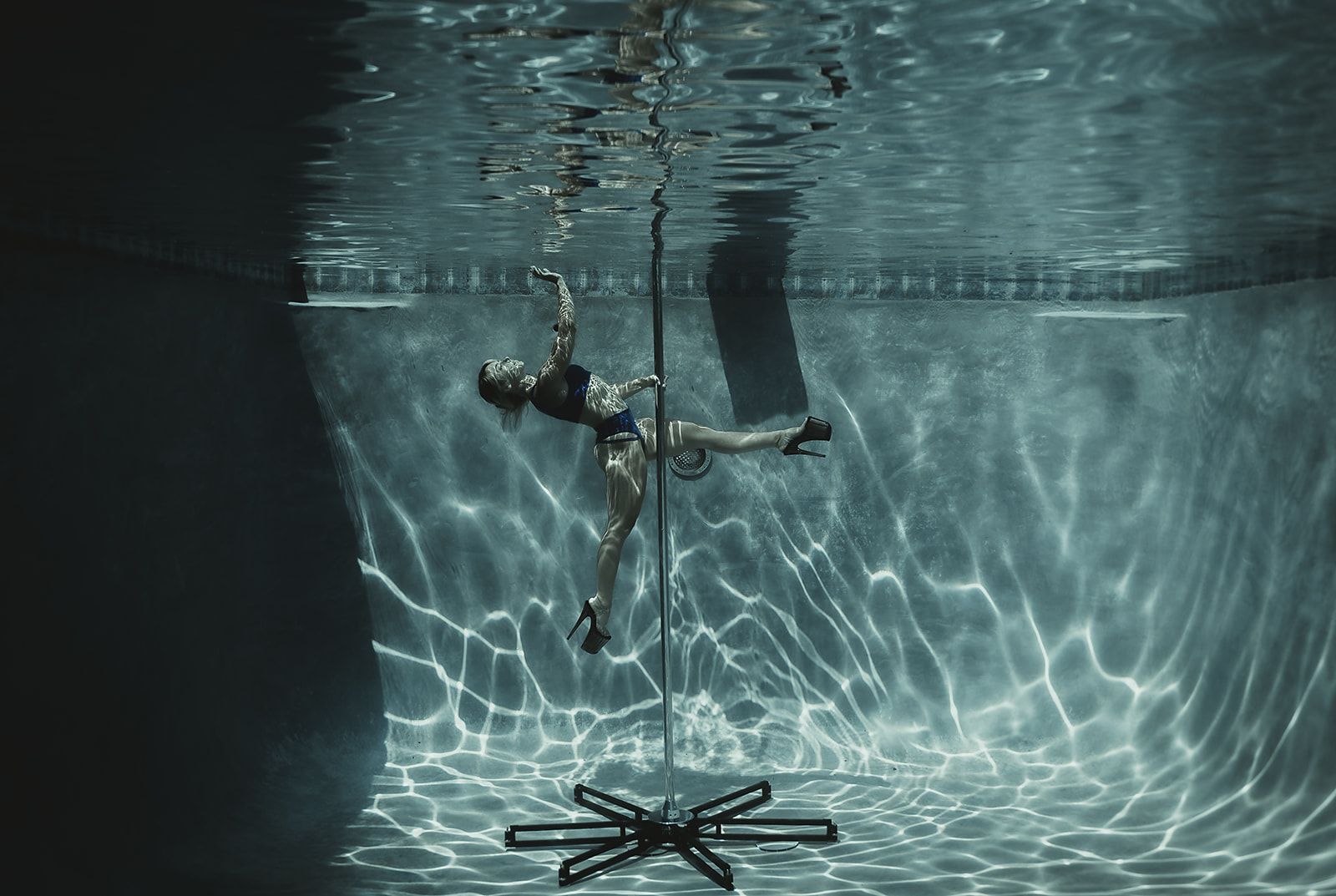 A woman is doing aerial acrobatics underwater in a swimming pool.