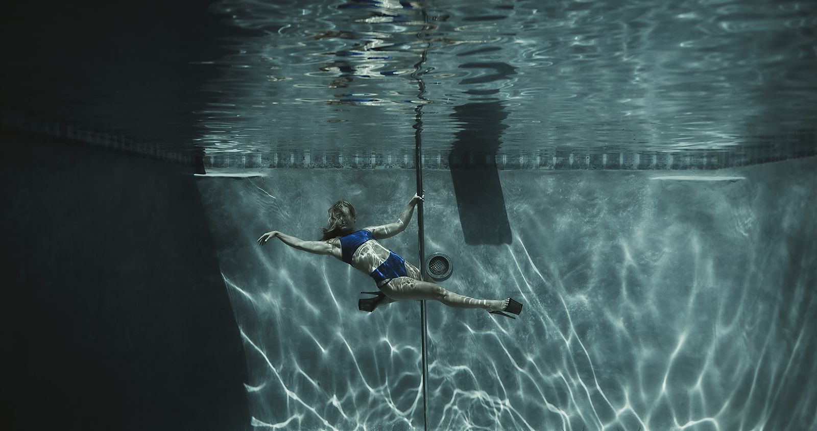 A woman is hanging from a pole underwater in a swimming pool.
