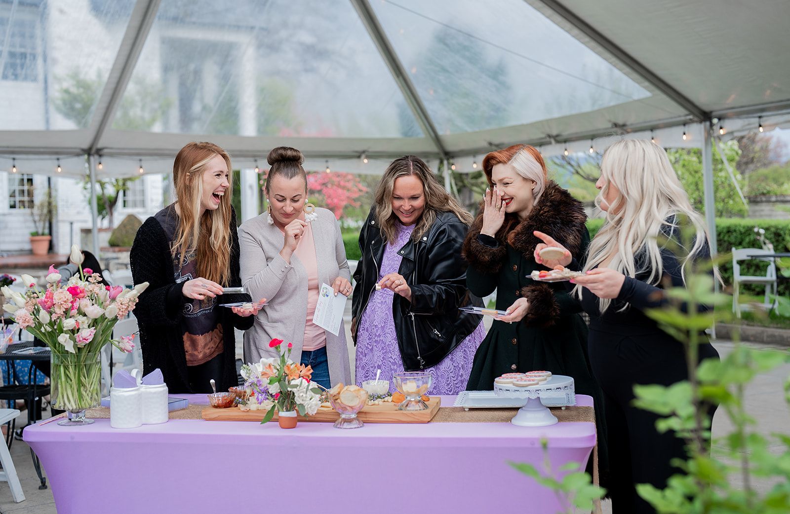 A group of women are standing around a table under a tent.