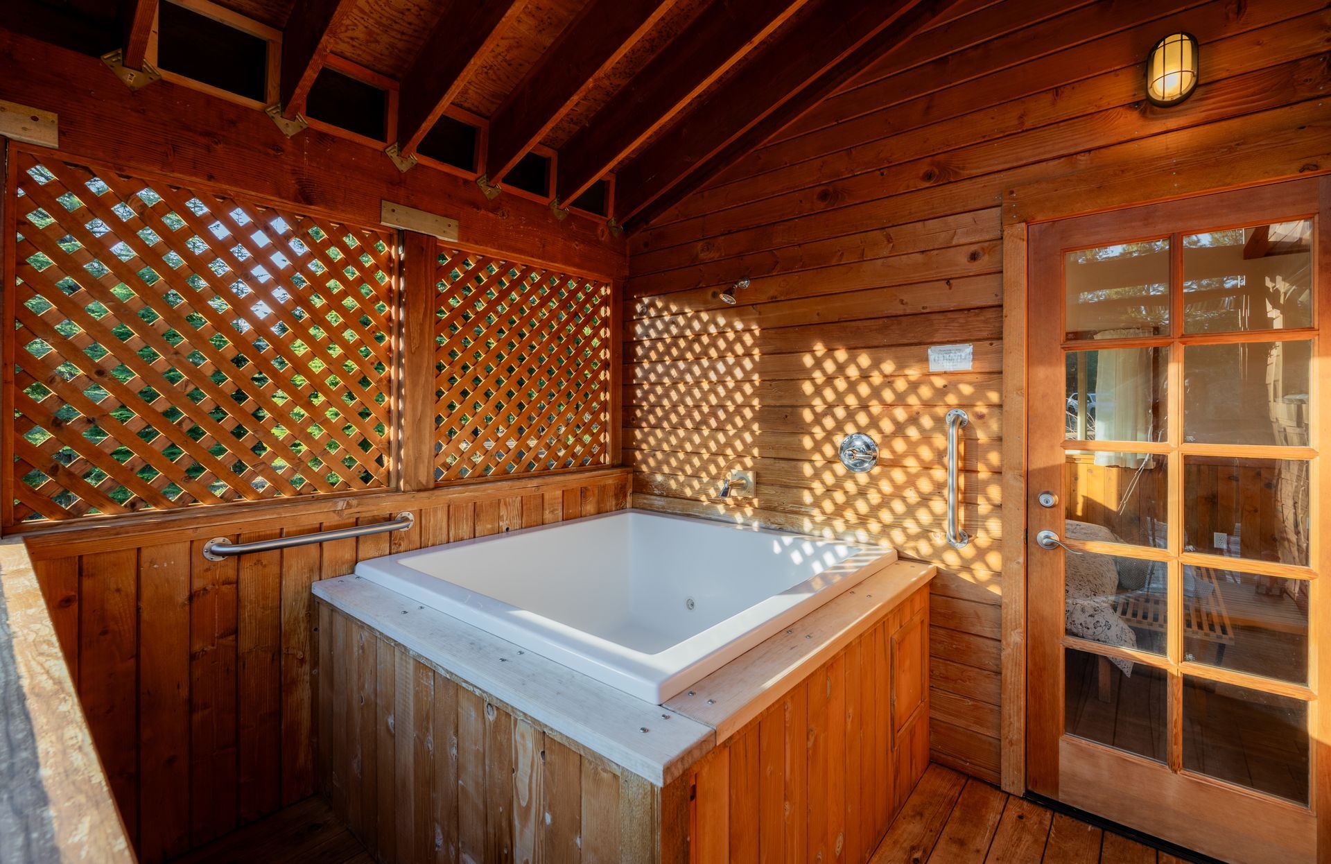 A jacuzzi tub is sitting under a wooden roof in a wooden cabin.