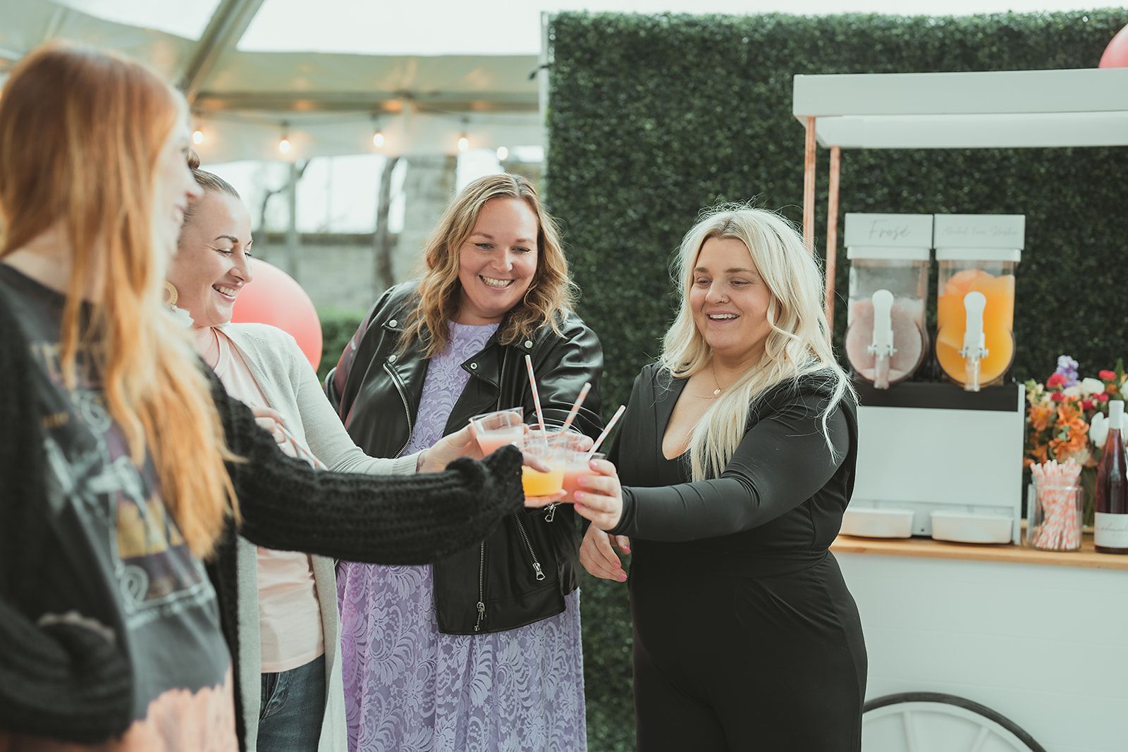 A group of women are standing next to each other toasting with drinks.