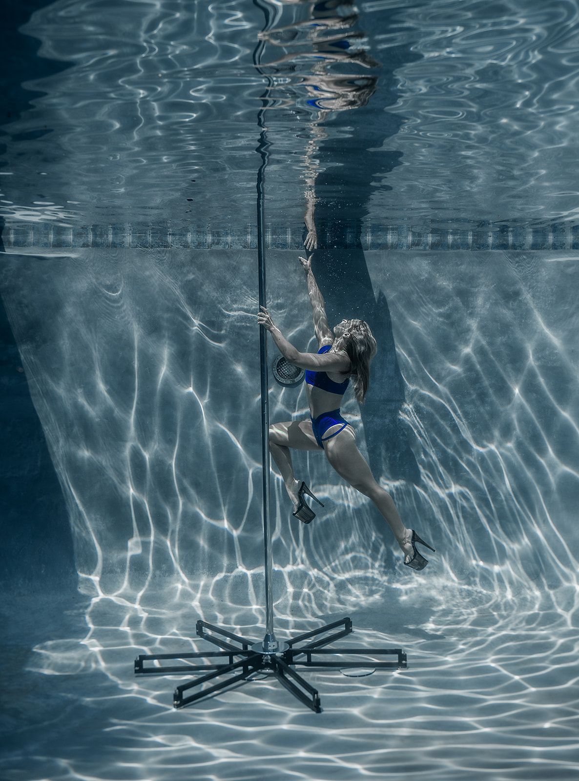 A woman is dancing on a pole underwater in a swimming pool.