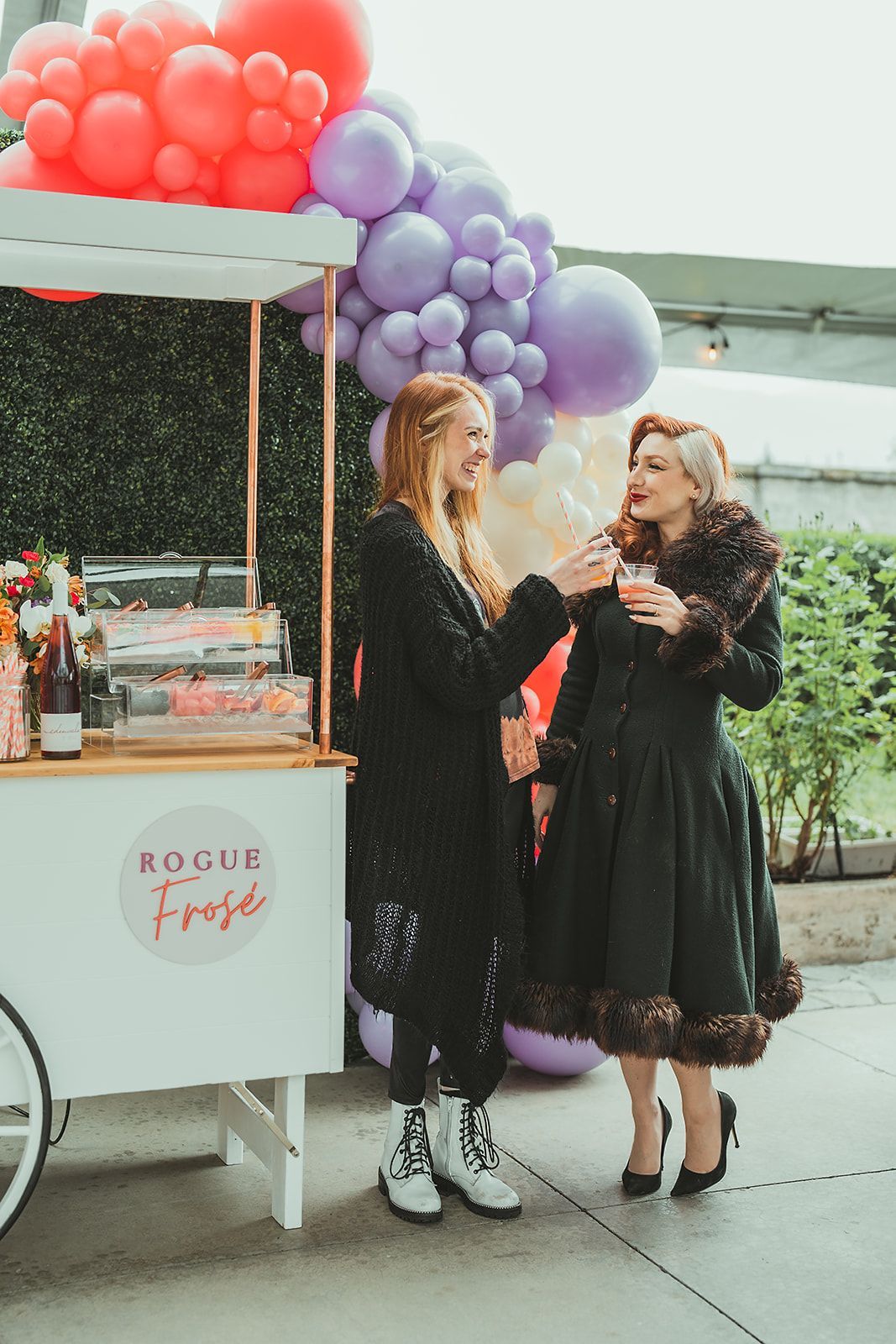 Two women are standing next to a cart with balloons on it.