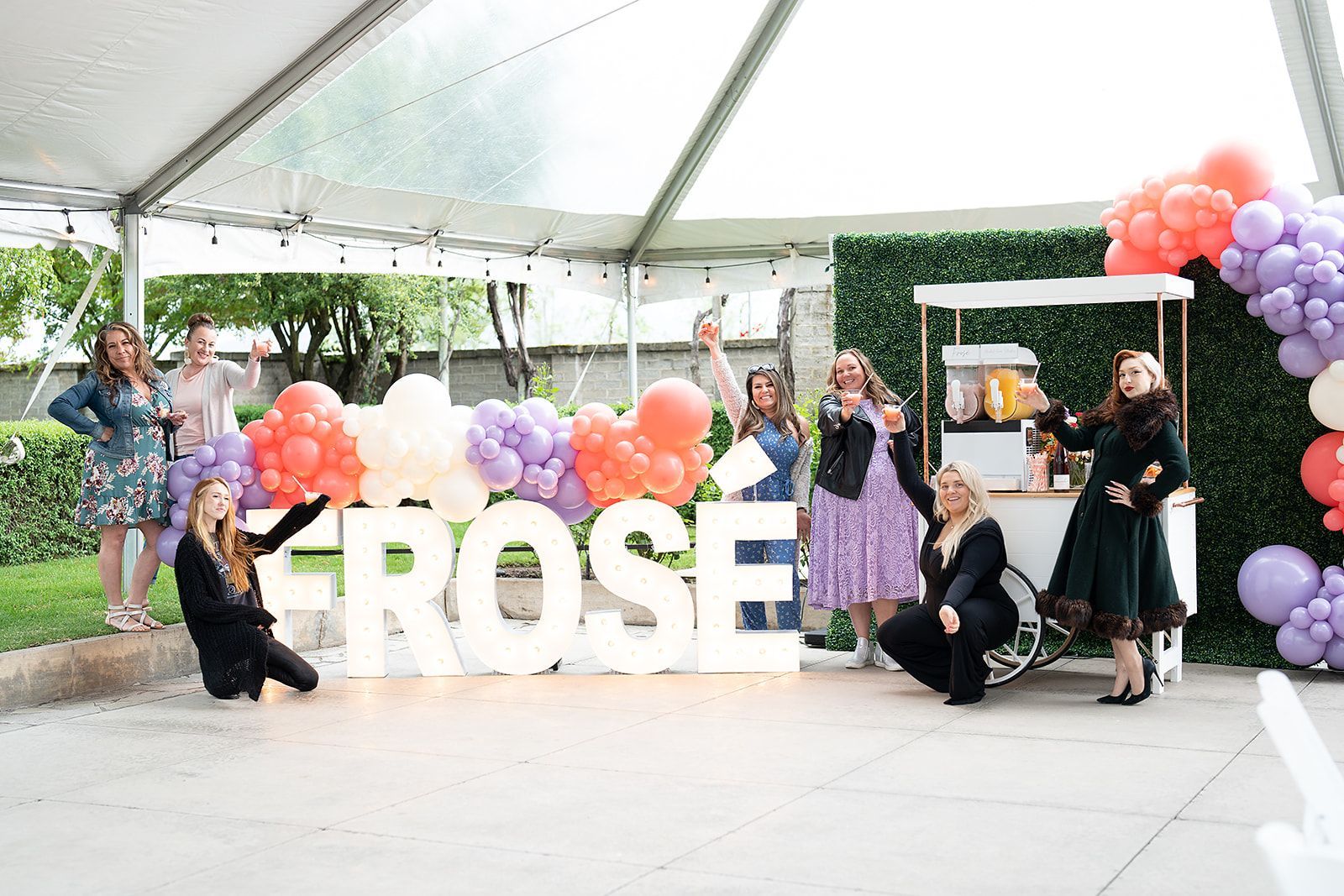 A group of women are posing for a picture in front of a large sign that says `` frose ''.