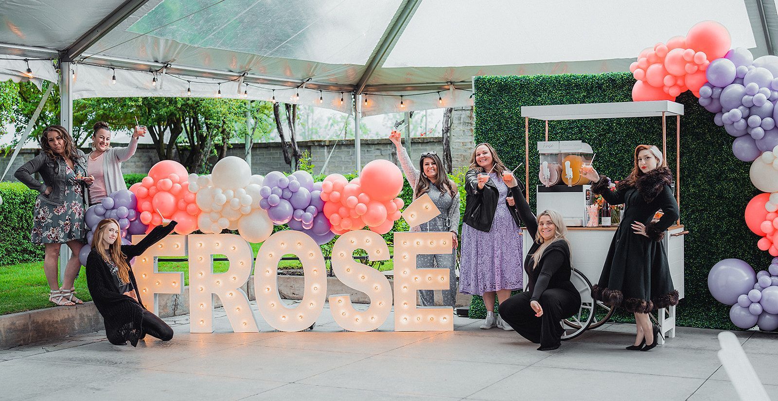 A group of women are posing for a picture in front of a large sign that says `` frose ''.
